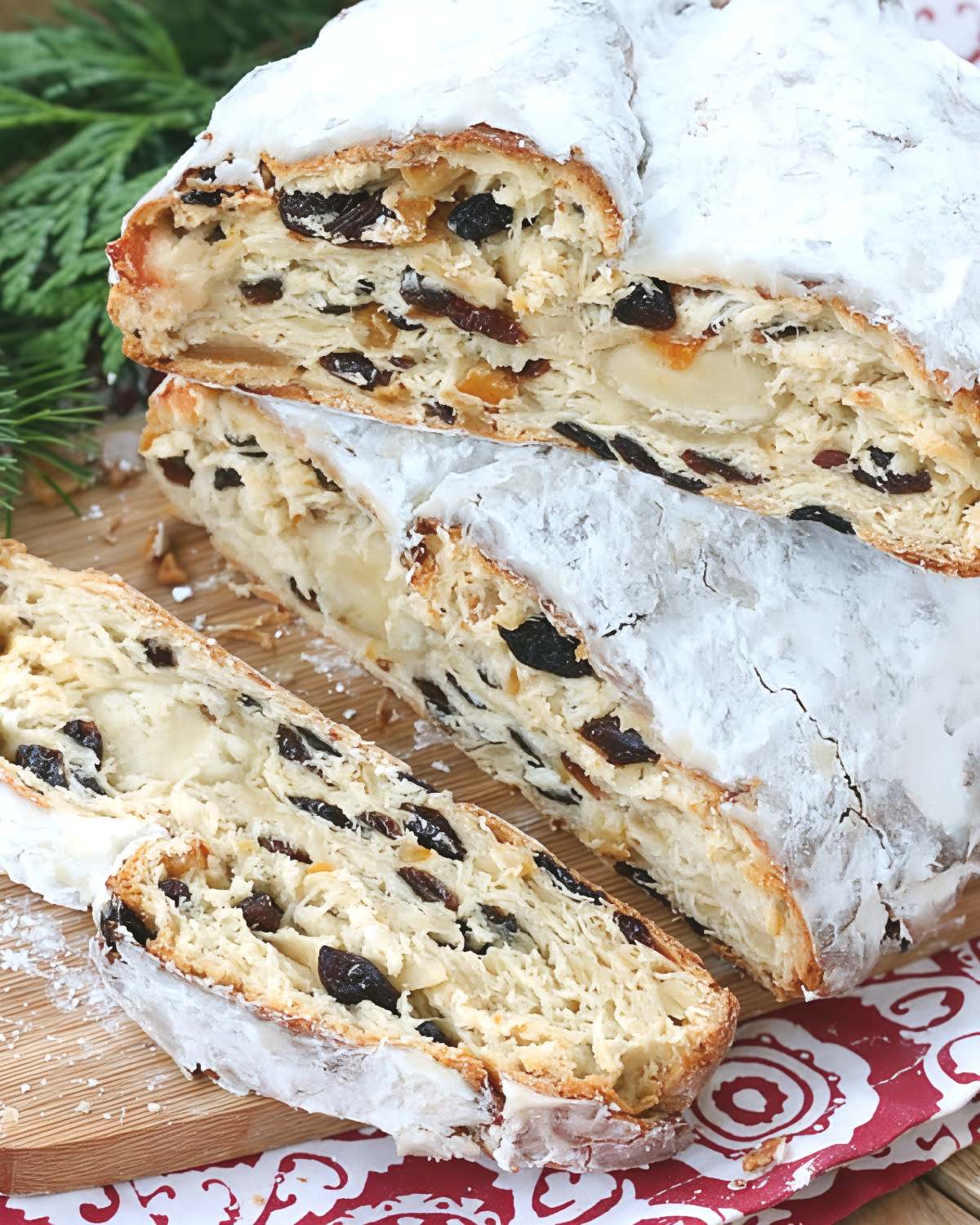 Traditional German Christstollen, a classic European Christmas dessert, is shown sliced on a wooden board with a heavy coating of powdered sugar.