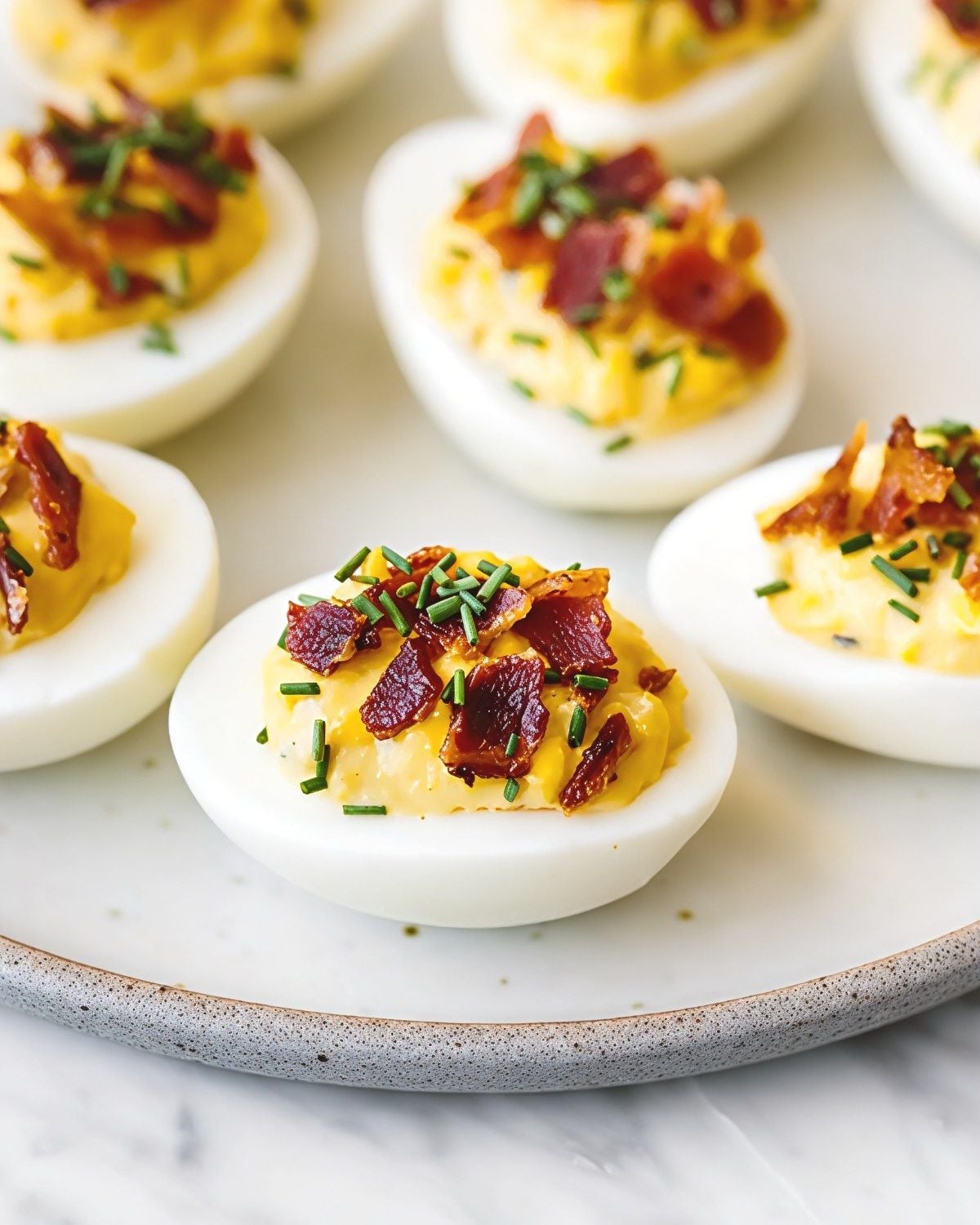 Creamy bacon deviled eggs topped with crispy chopped bacon and fresh chives arranged on a white serving platter, perfect as quick and easy last minute potluck ideas.