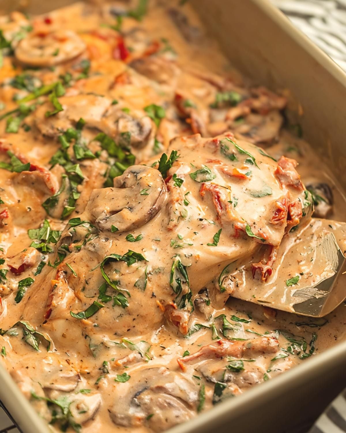 Creamy baked Tuscan chicken with mushrooms and sun-dried tomatoes in a casserole dish, a quick and easy dump and bake recipe for dinner.