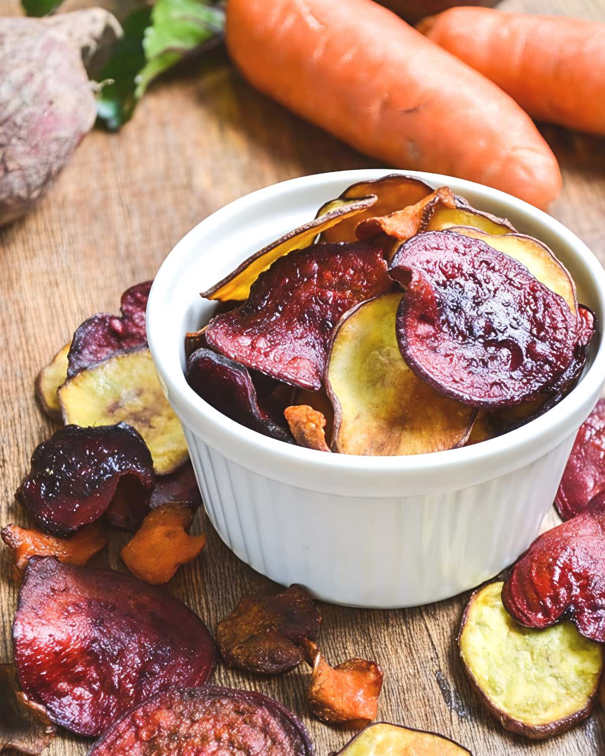 Colorful baked vegetable chips made from beets, sweet potatoes, and root vegetables served in a white ramekin on a rustic wooden table for a healthy, light Thanksgiving appetizer.
