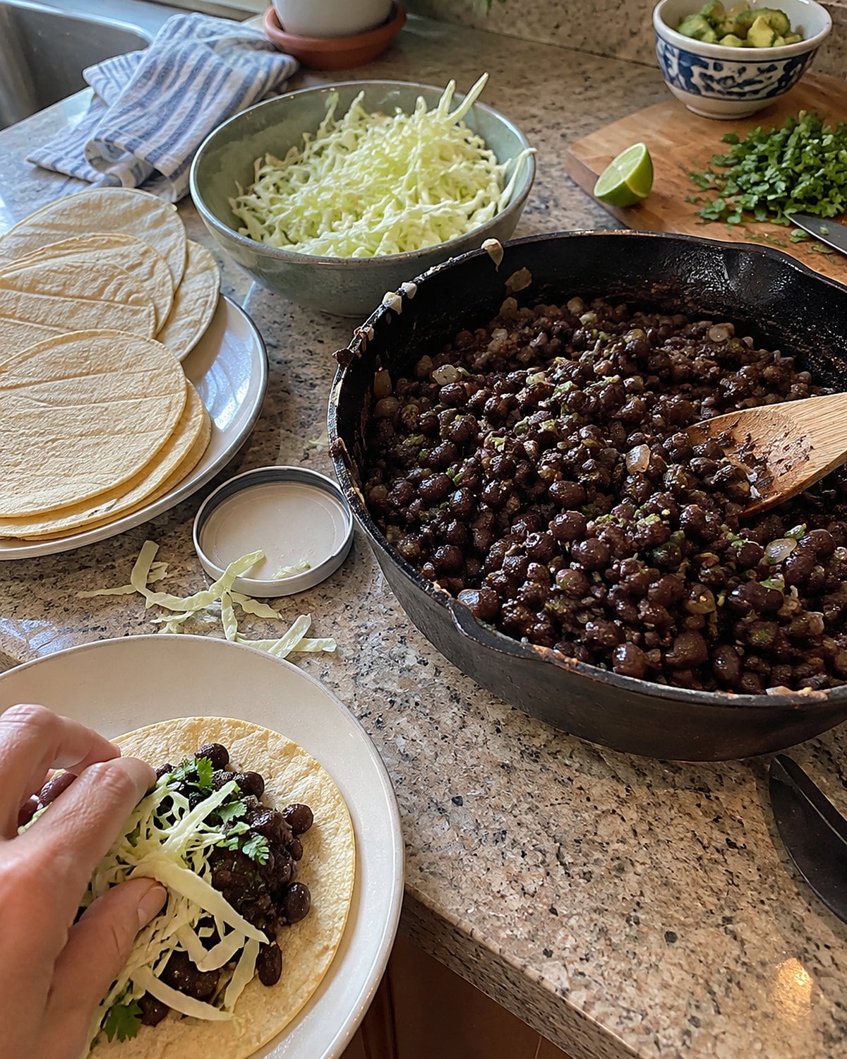 Black bean filling sits in a skillet beside a small pile of shredded cabbage and loose tortillas.