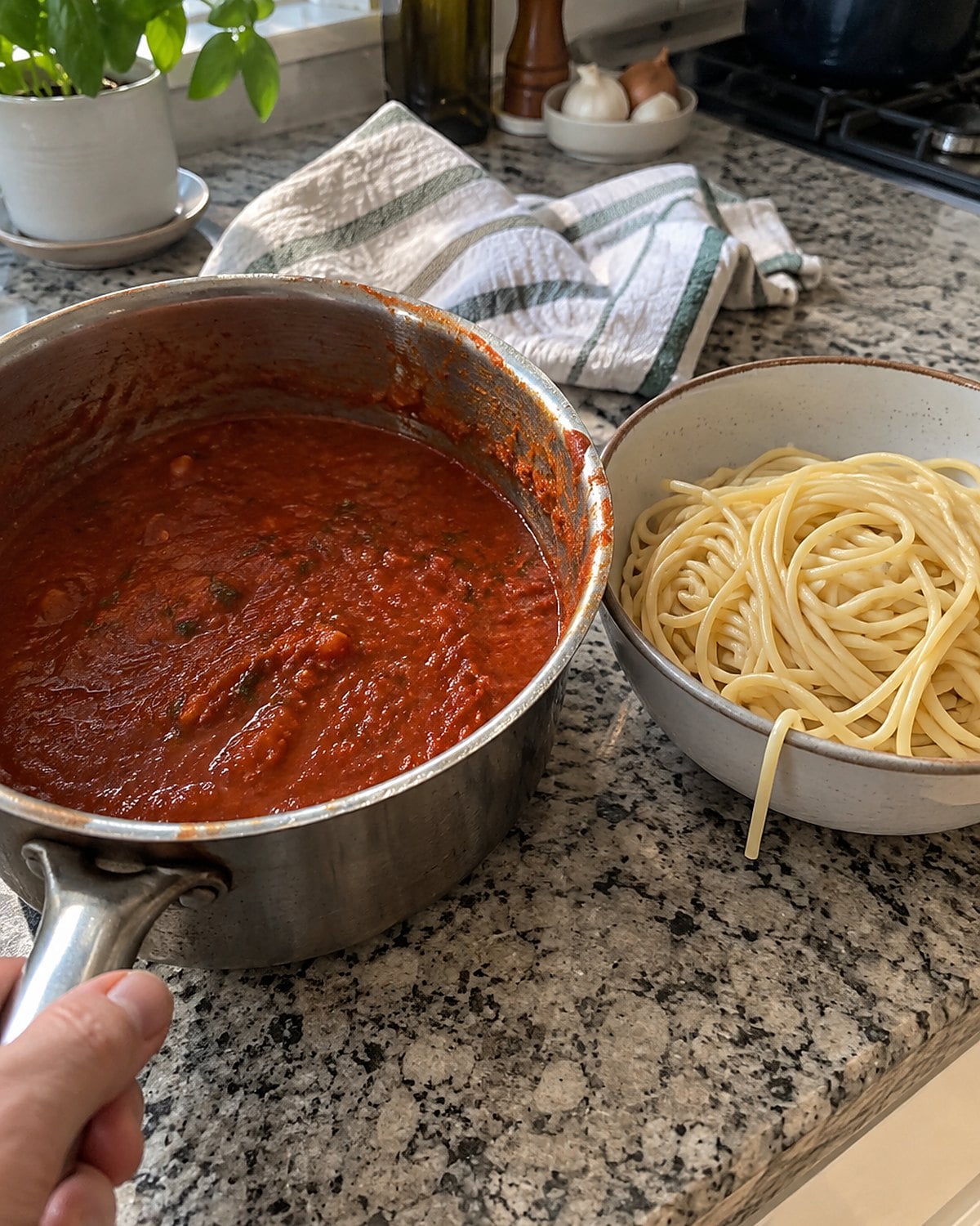A saucepan of tomato sauce sits beside a small bowl of plain cooked pasta on the counter.