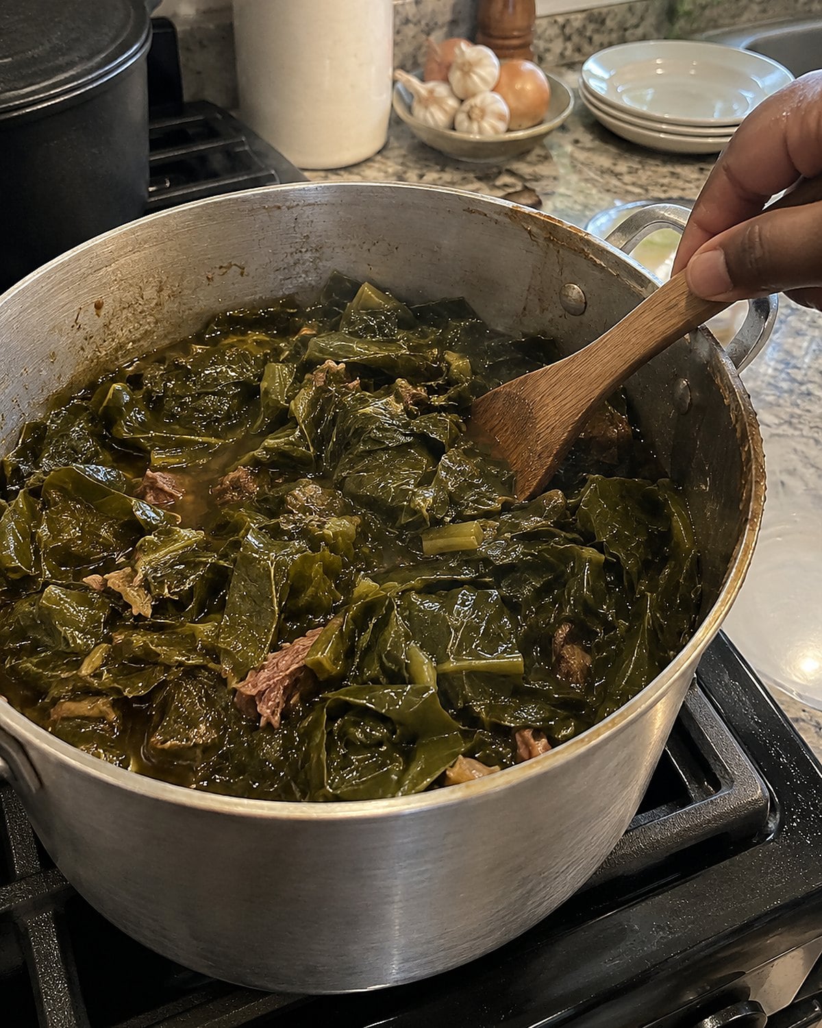 Collard greens sit in a dented pot with their cooking liquid visible around the leaves.