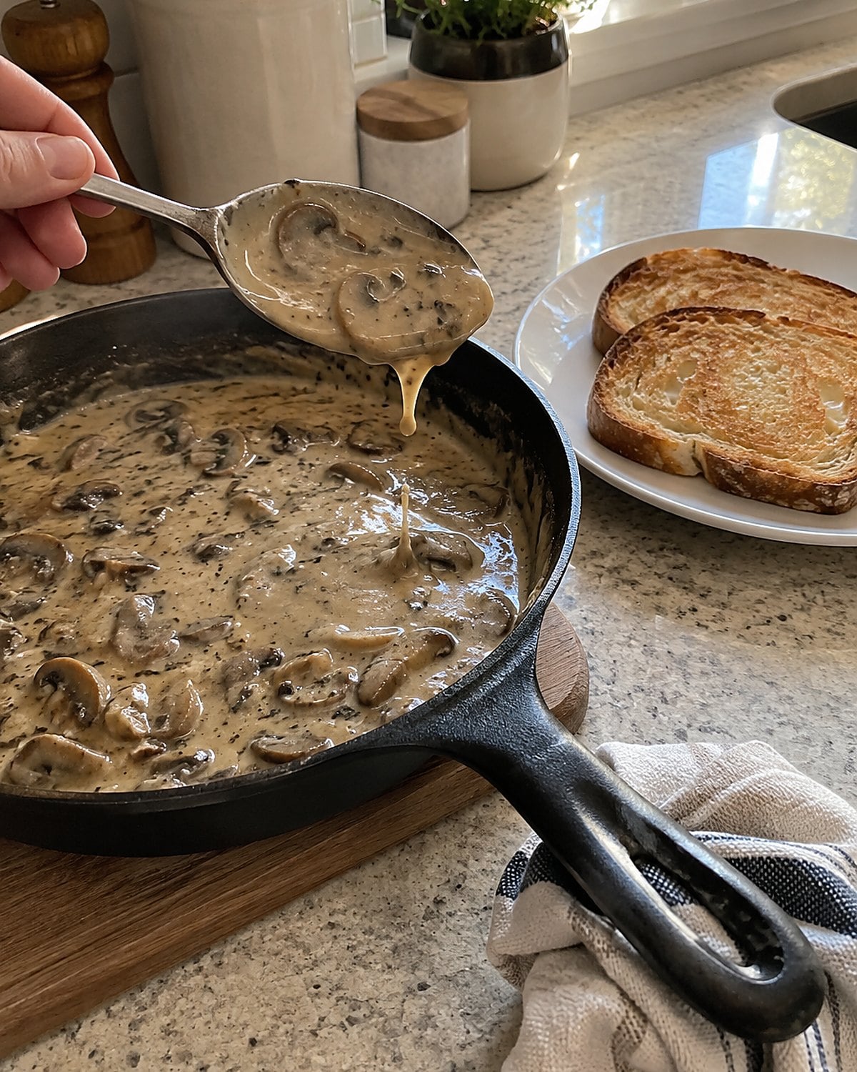 Mushroom gravy coats the back of a spoon over a skillet, with fresh toast waiting on a plate.
