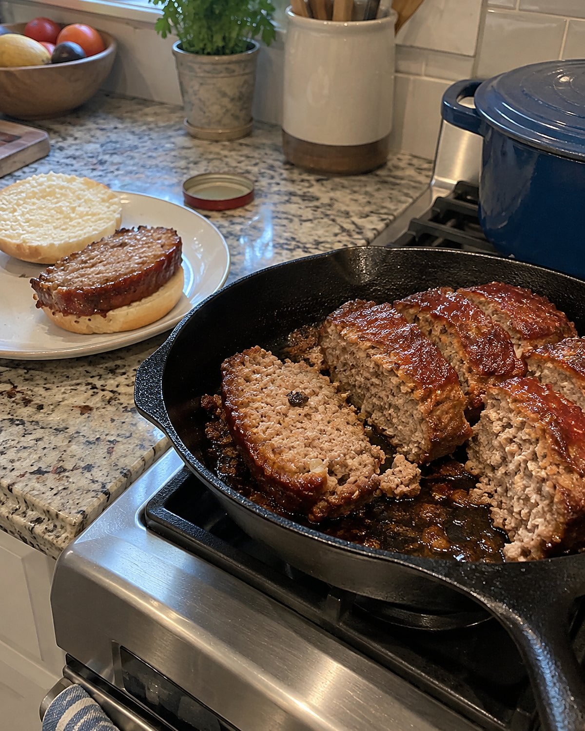 Thick slices of meatloaf brown in a cast-iron skillet beside an open sandwich bun.