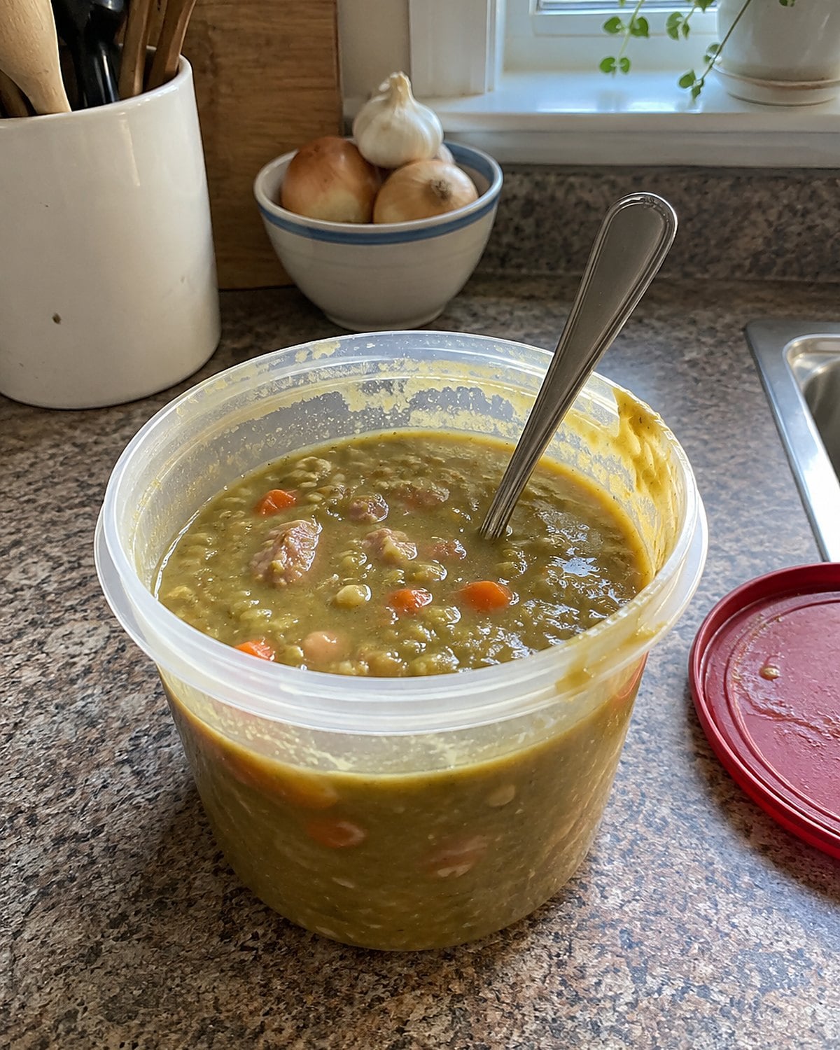 A spoon stands in a thick container of split pea soup on the kitchen counter.