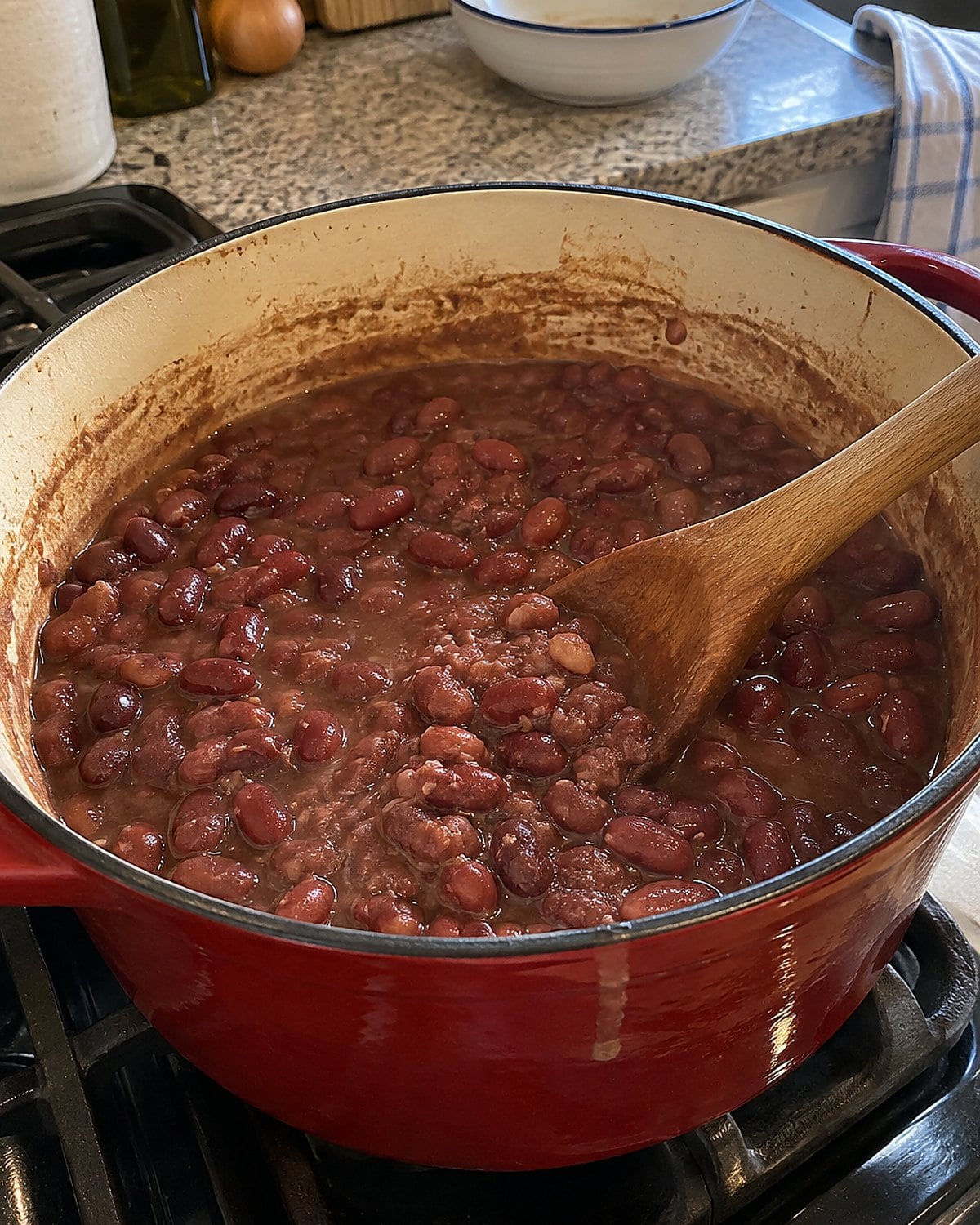 A wooden spoon rests in a pot of red beans, with a few mashed beans visible against the side.