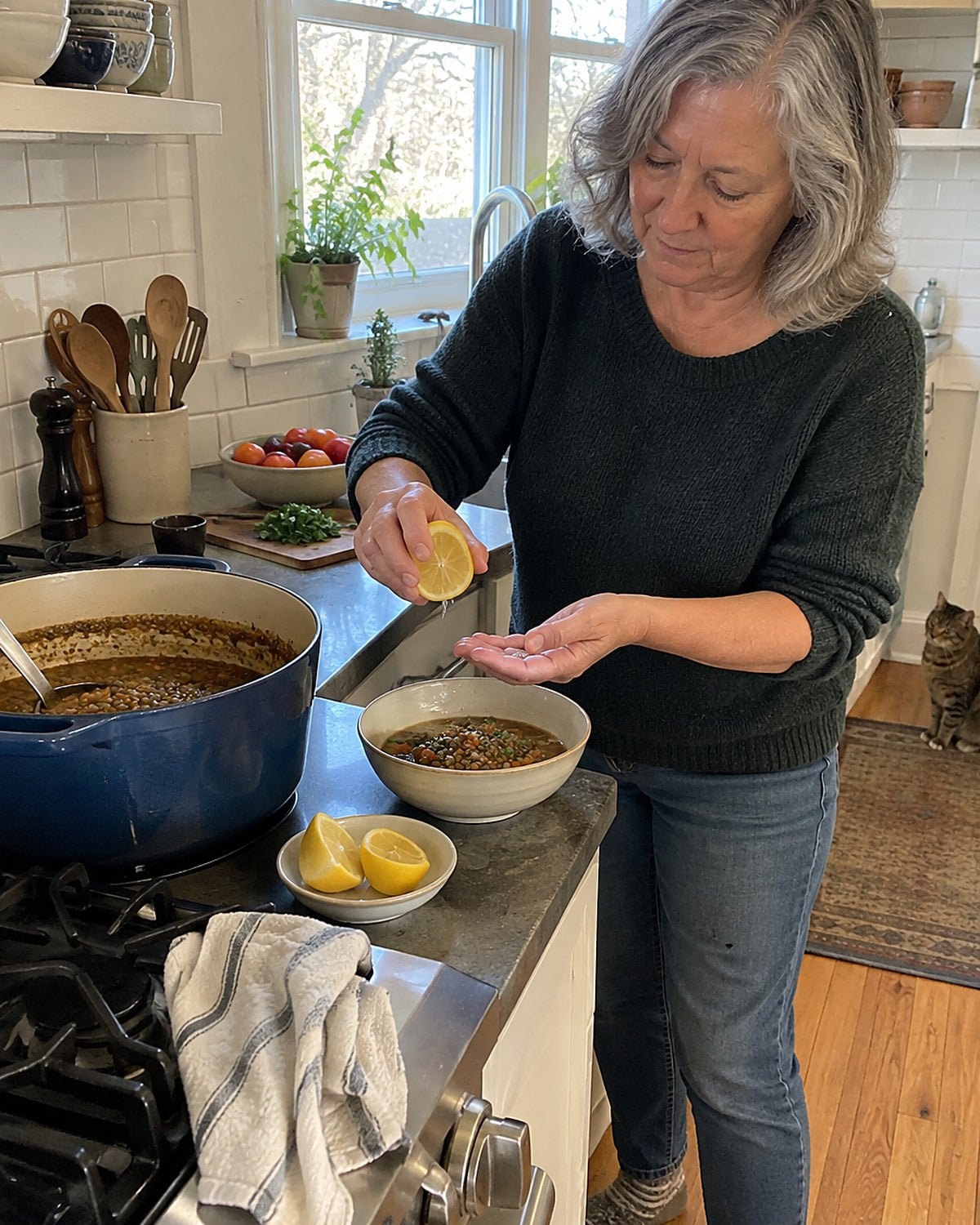 A hand squeezes a lemon over lentil soup in a worn bowl beside the stove.