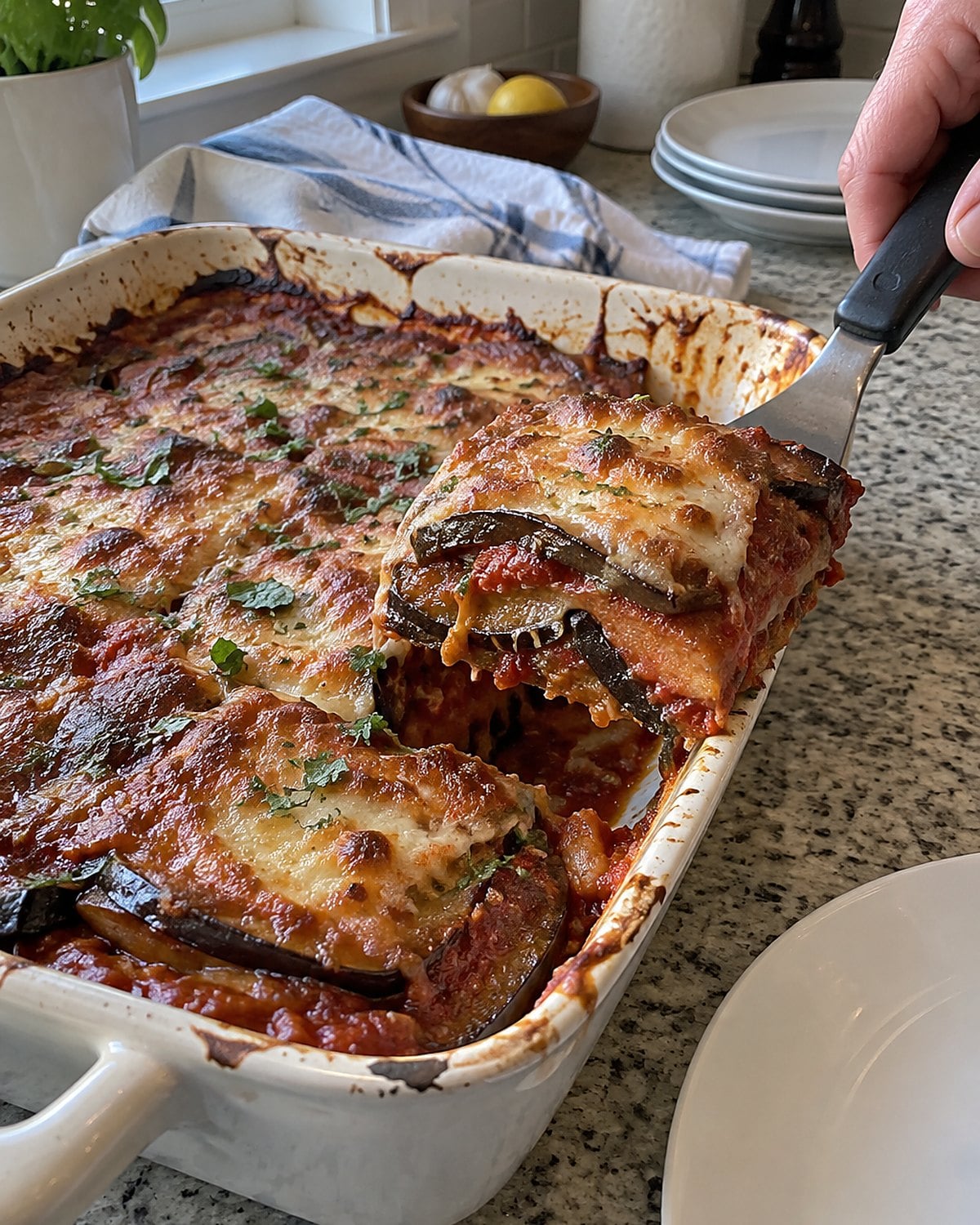 A corner of eggplant Parmesan lifts from a baking dish, showing a crisp exposed edge.