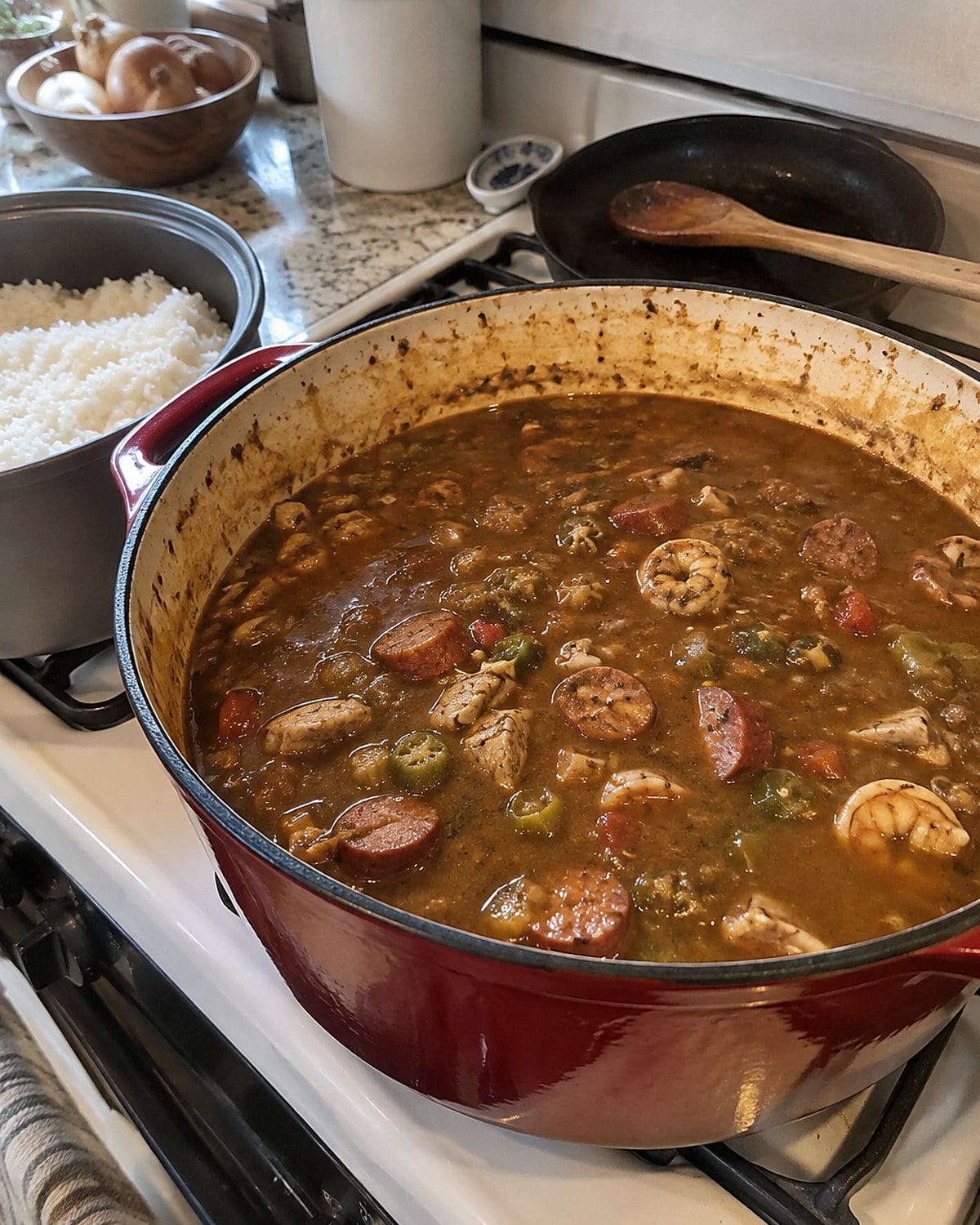 A pot of gumbo sits on the stove beside a separate container of white rice.