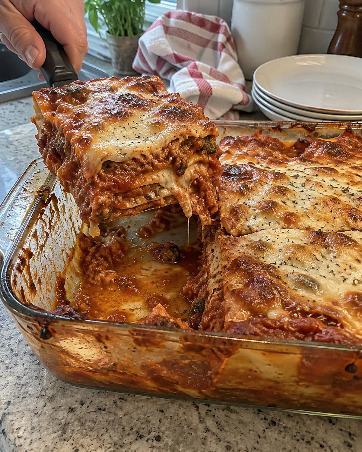 A spatula lifts a firm square of lasagna from a glass baking dish with sauce along the rim.