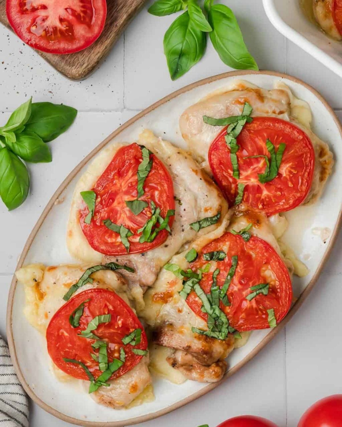 Top-down view of tender chicken breasts layered with melted cheese, tomato slices, and chopped fresh basil, featured as a delicious high protein low carb recipes dinner.