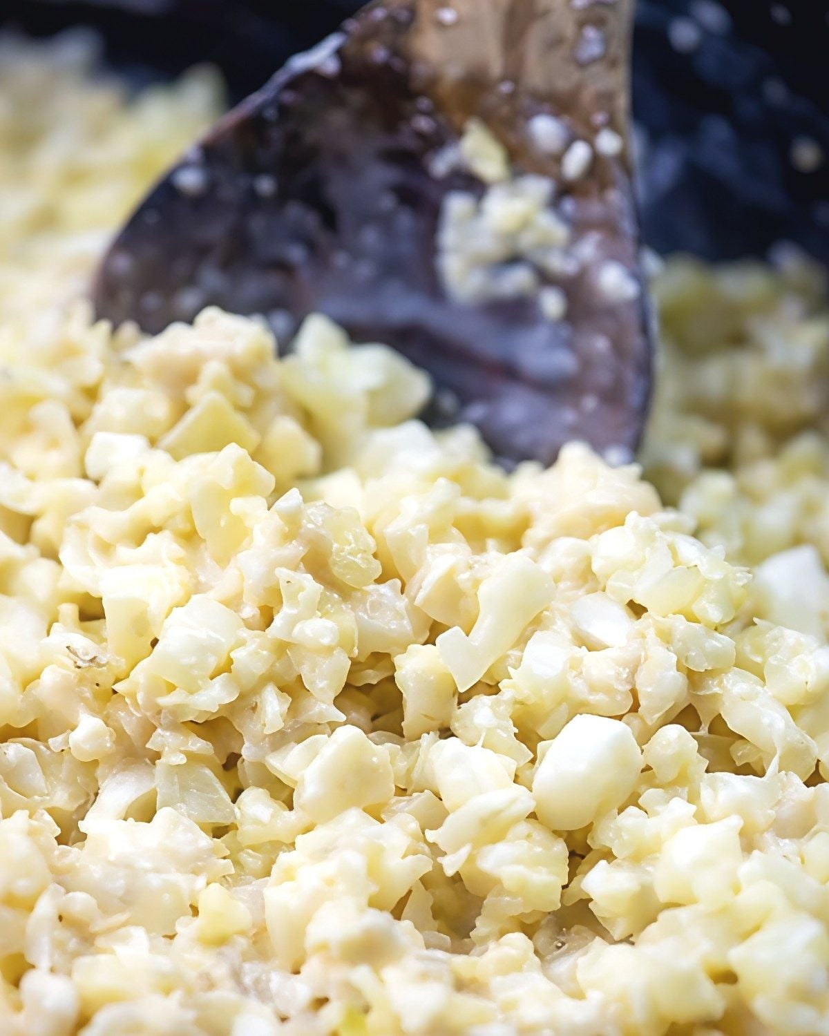 A close-up shot shows a wooden spoon stirring creamy low-carb cauliflower risotto in a pot, making a delicious option for keto thanksgiving sides.