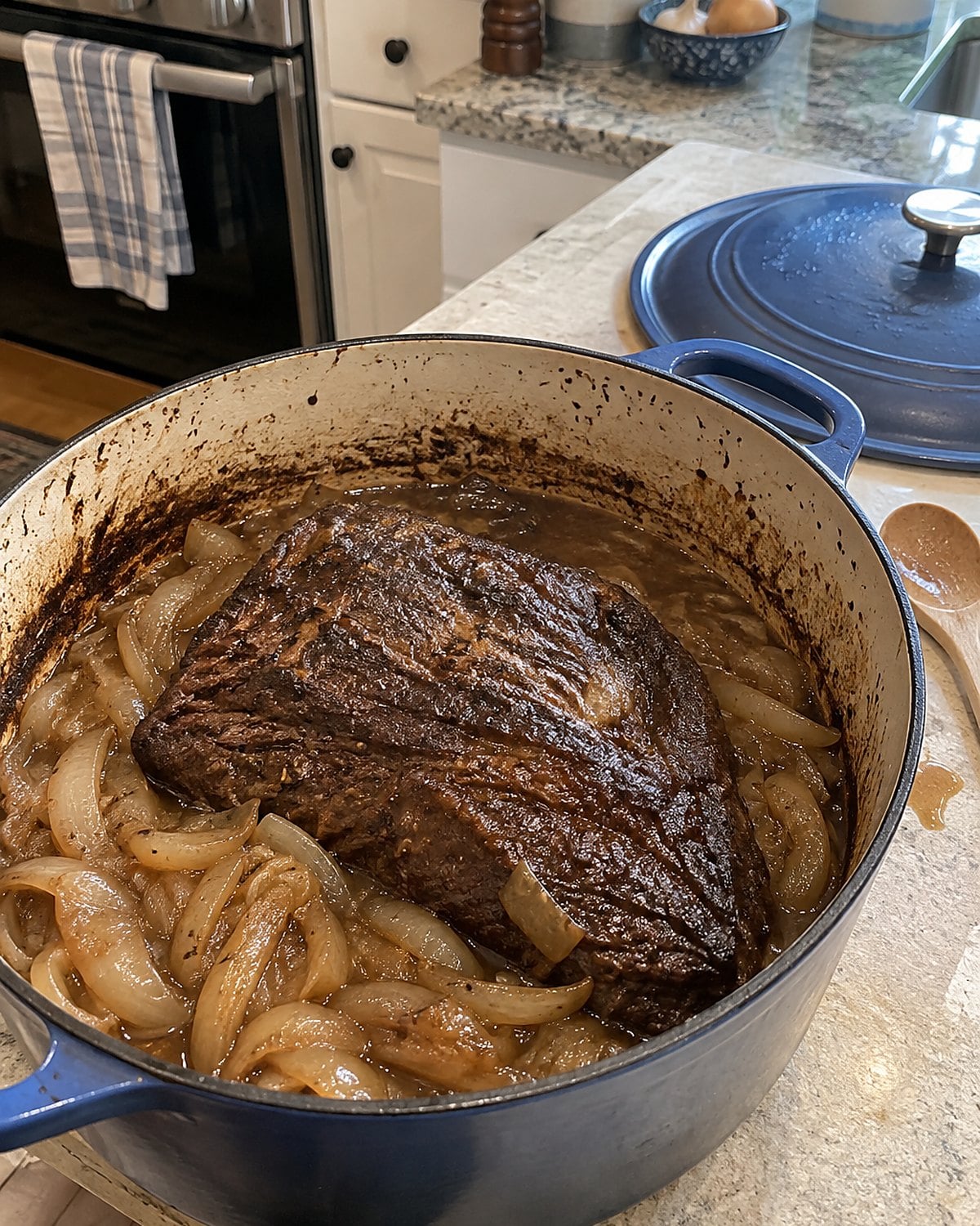 A brisket in a Dutch oven with onions around it and the lid resting nearby.