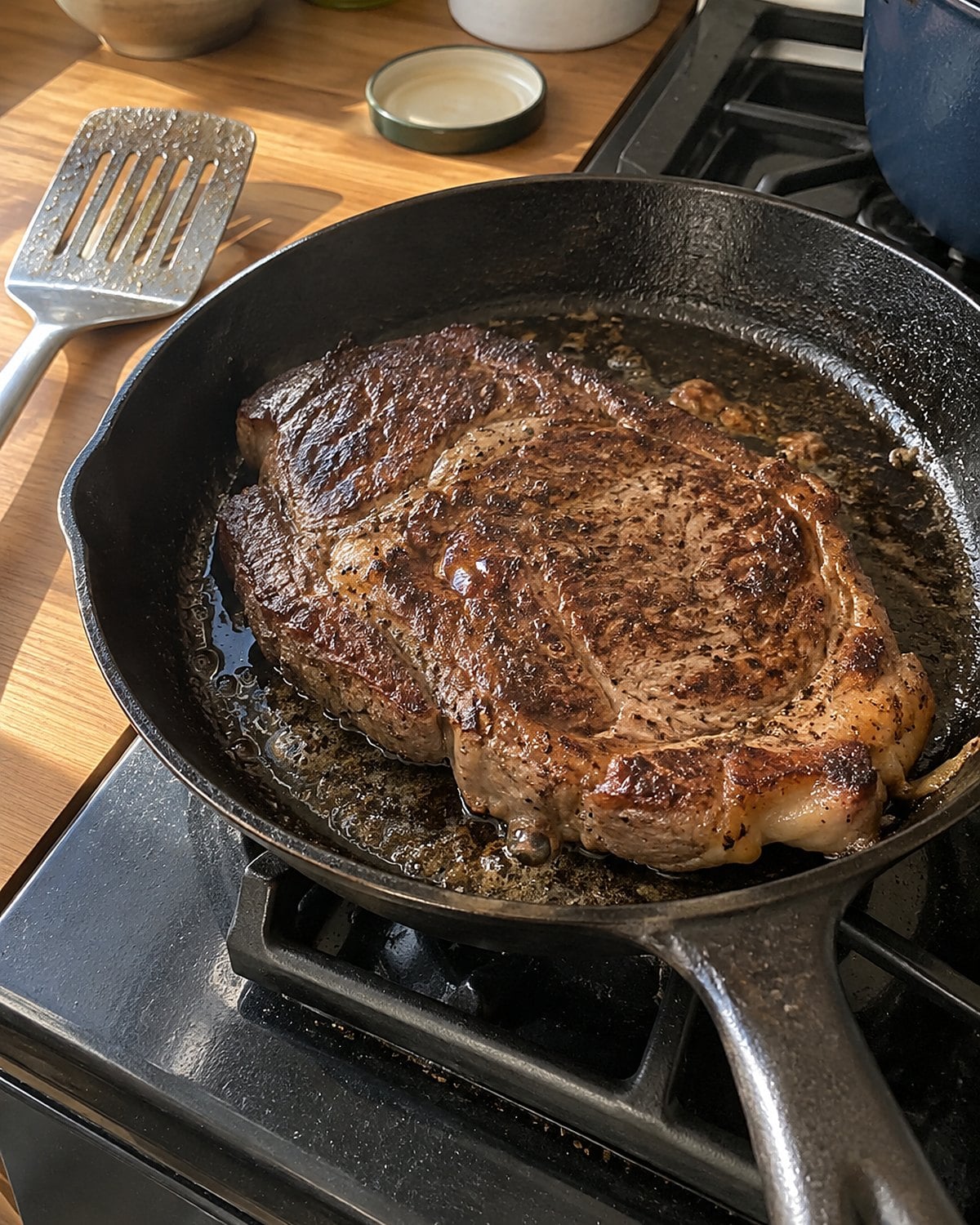 One browned chuck eye steak resting in a skillet beside a spatula on the stove.