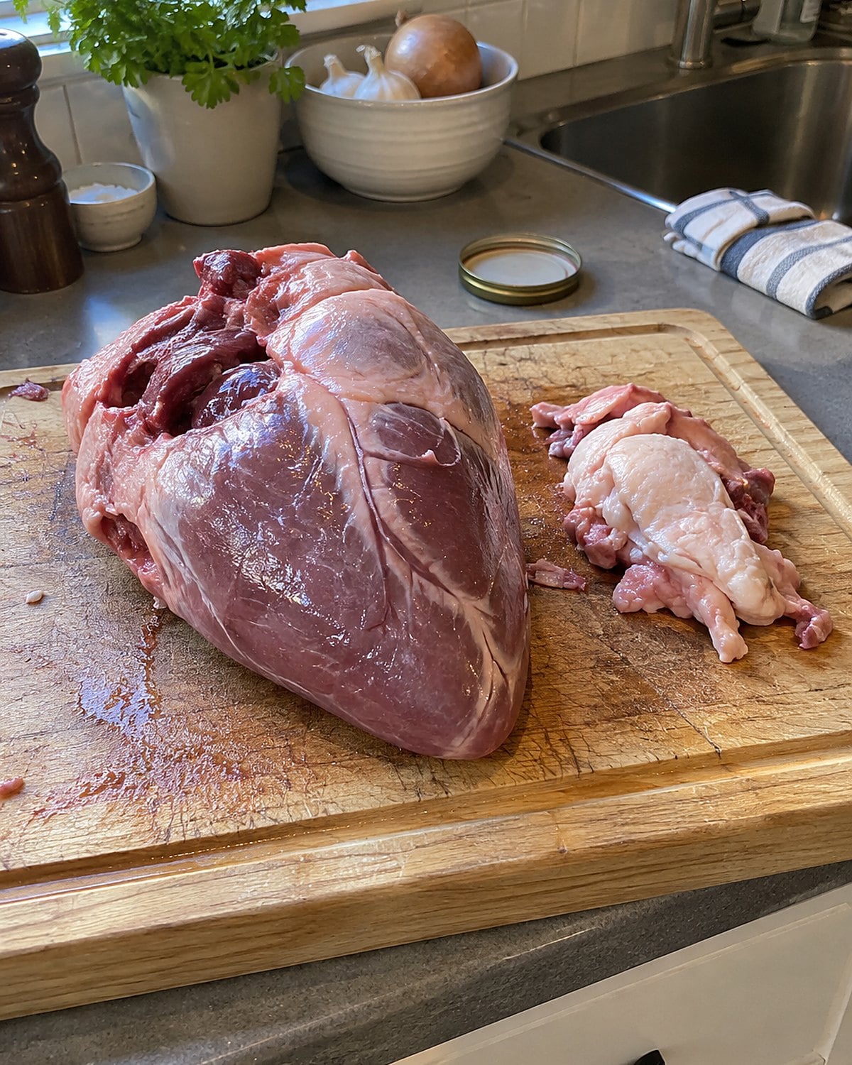 A trimmed beef heart and a small pile of firm white trimmings on a cutting board.