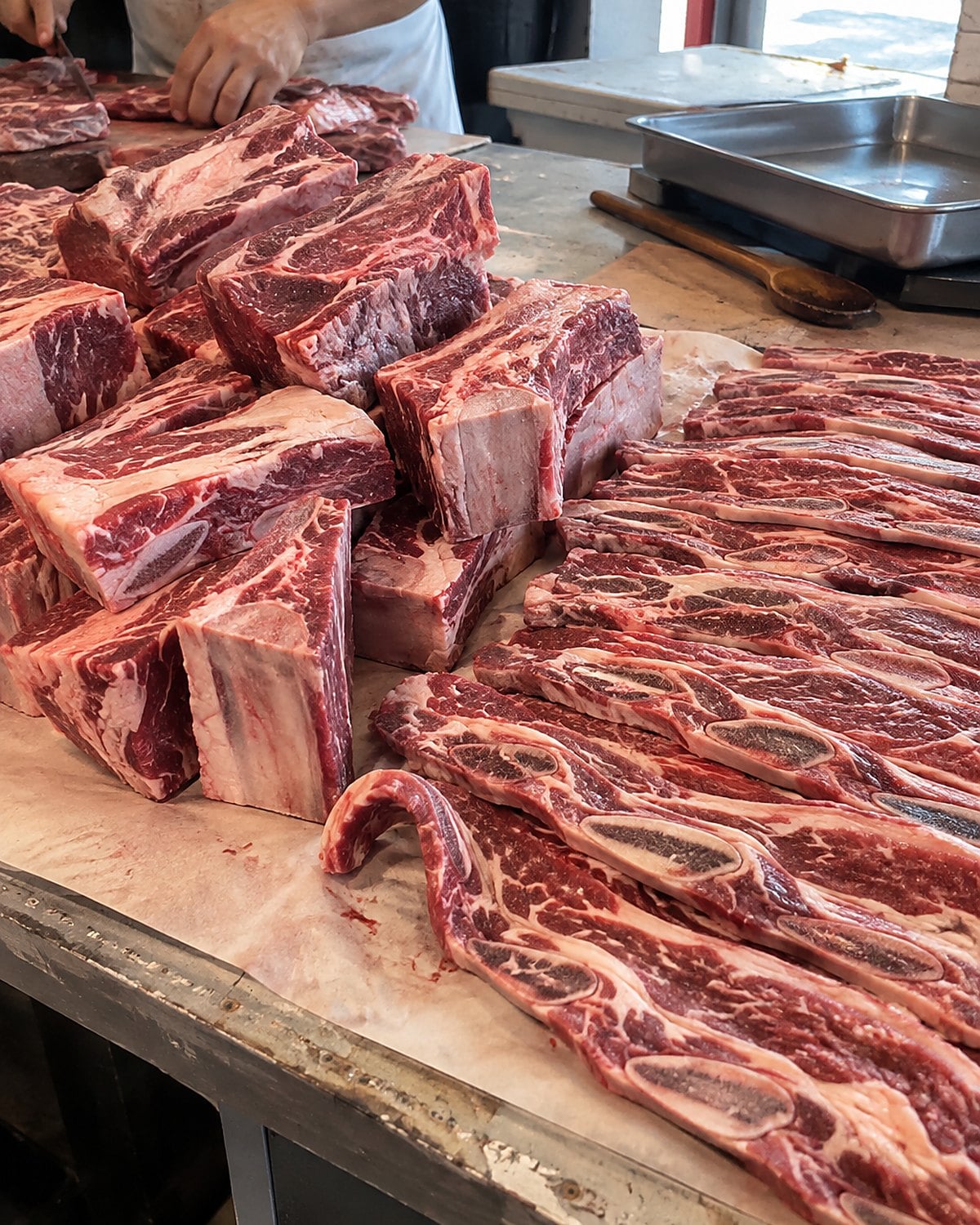 Thick short ribs and thin flanken strips side by side on butcher paper at a market stall.