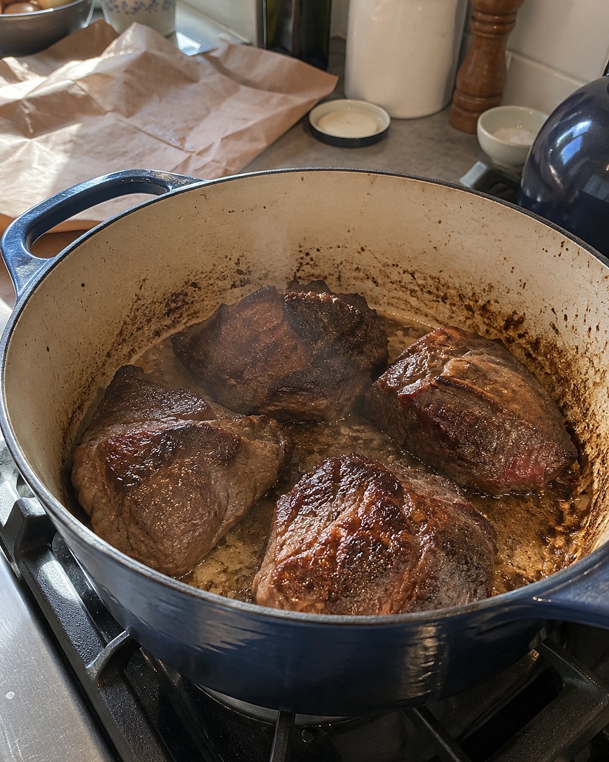 Beef cheeks browning in a heavy Dutch oven, with a folded butcher-paper wrapper on the counter.