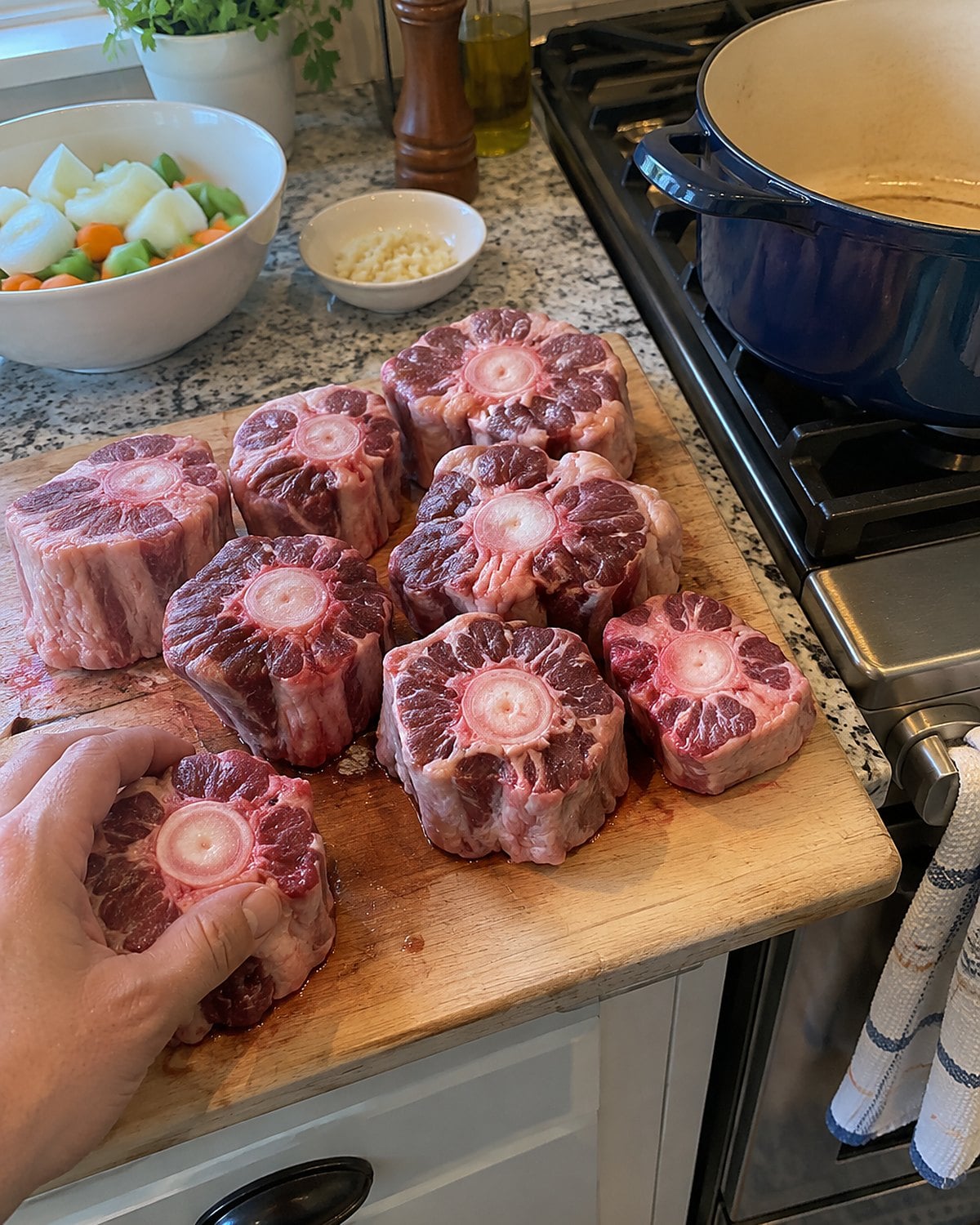 Crosscut oxtail pieces on a worn cutting board beside a deep pot on a home stove.