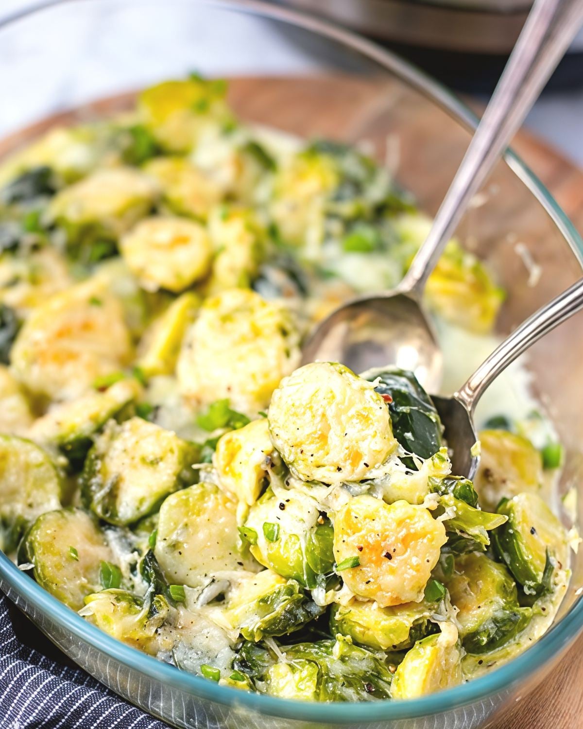 A serving spoon scooping up cheesy, creamy Brussels sprouts topped with melted cheese from a glass baking dish, making it a perfect Thanksgiving vegetable side dish.