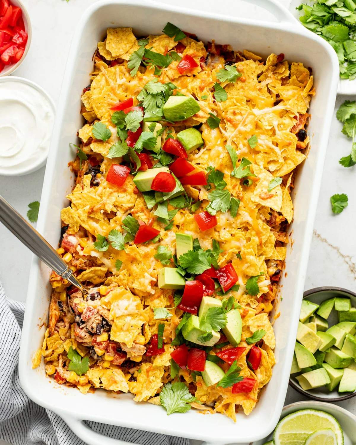 Chicken taco casserole topped with tortilla chips, avocado, and tomatoes, a quick dump and bake recipe for dinner.