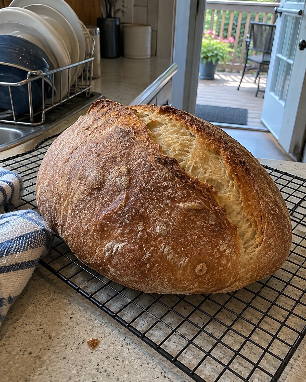 A loaf of bread cooling on a wire rack by an open porch door.