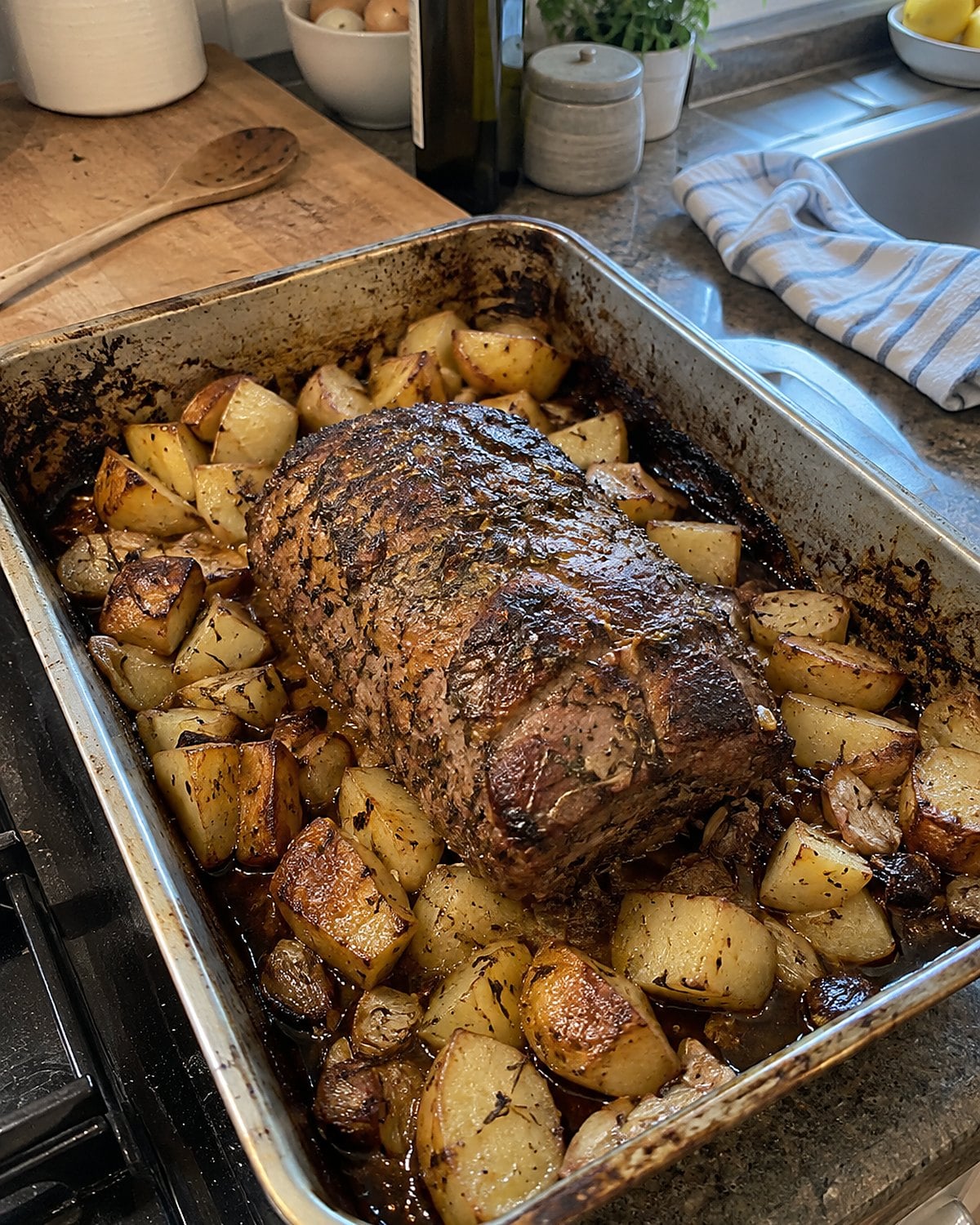 Unevenly cut potatoes browning around a roast in a worn metal pan.