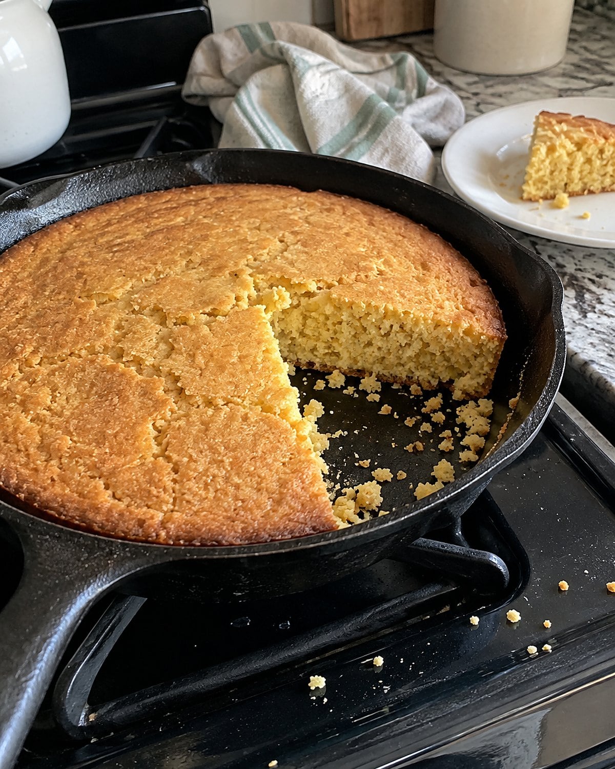 A cast-iron skillet of cornbread with a wedge cut out and crumbs on the stove.