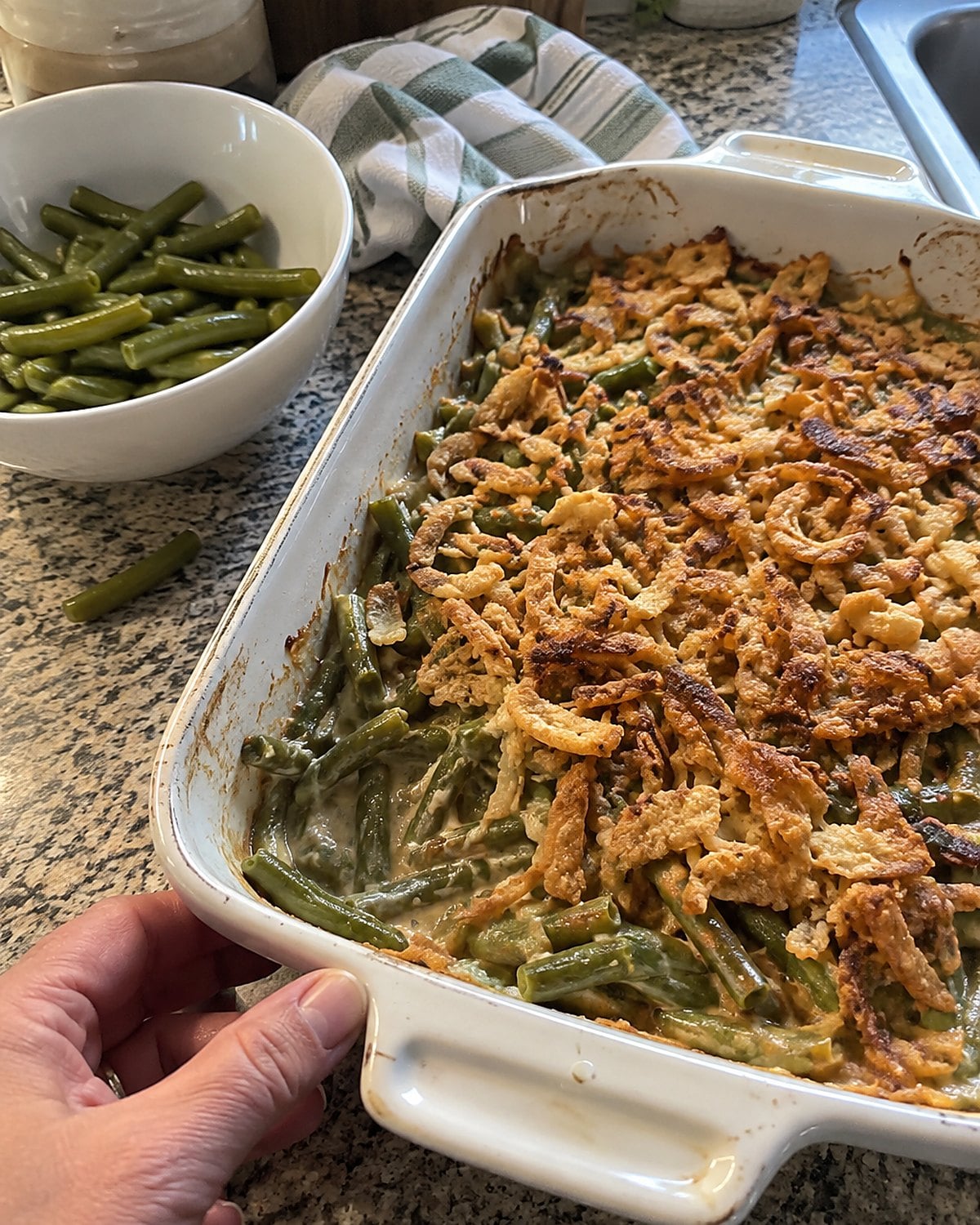 A baking dish of green bean casserole with crisp fried onions beside a bowl of plain beans.