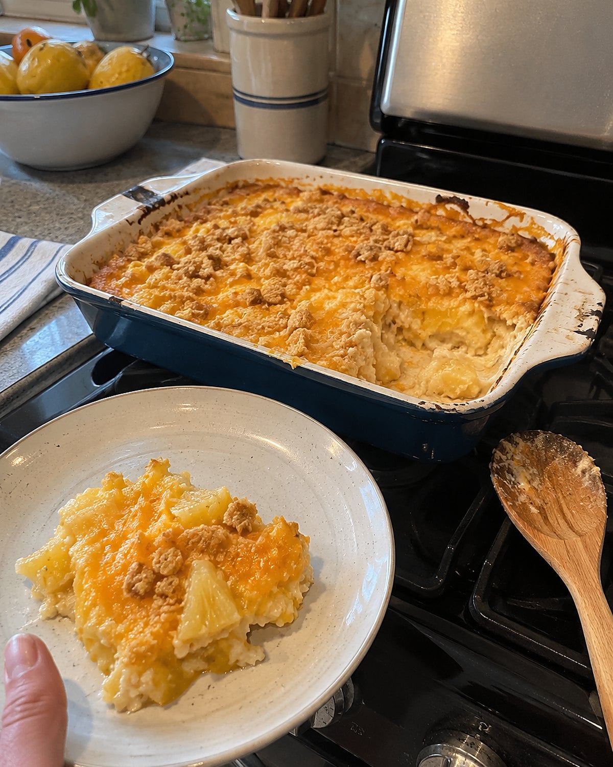 A spoonful missing from pineapple cheese casserole in a chipped baking dish on the stove.
