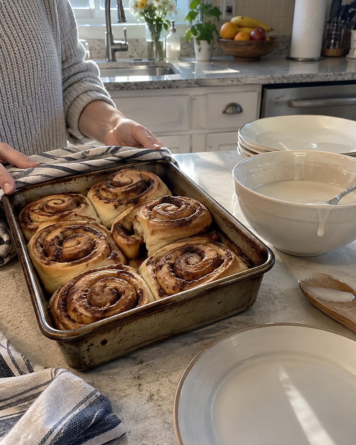 A pan of cinnamon rolls with icing in a separate bowl beside breakfast plates.
