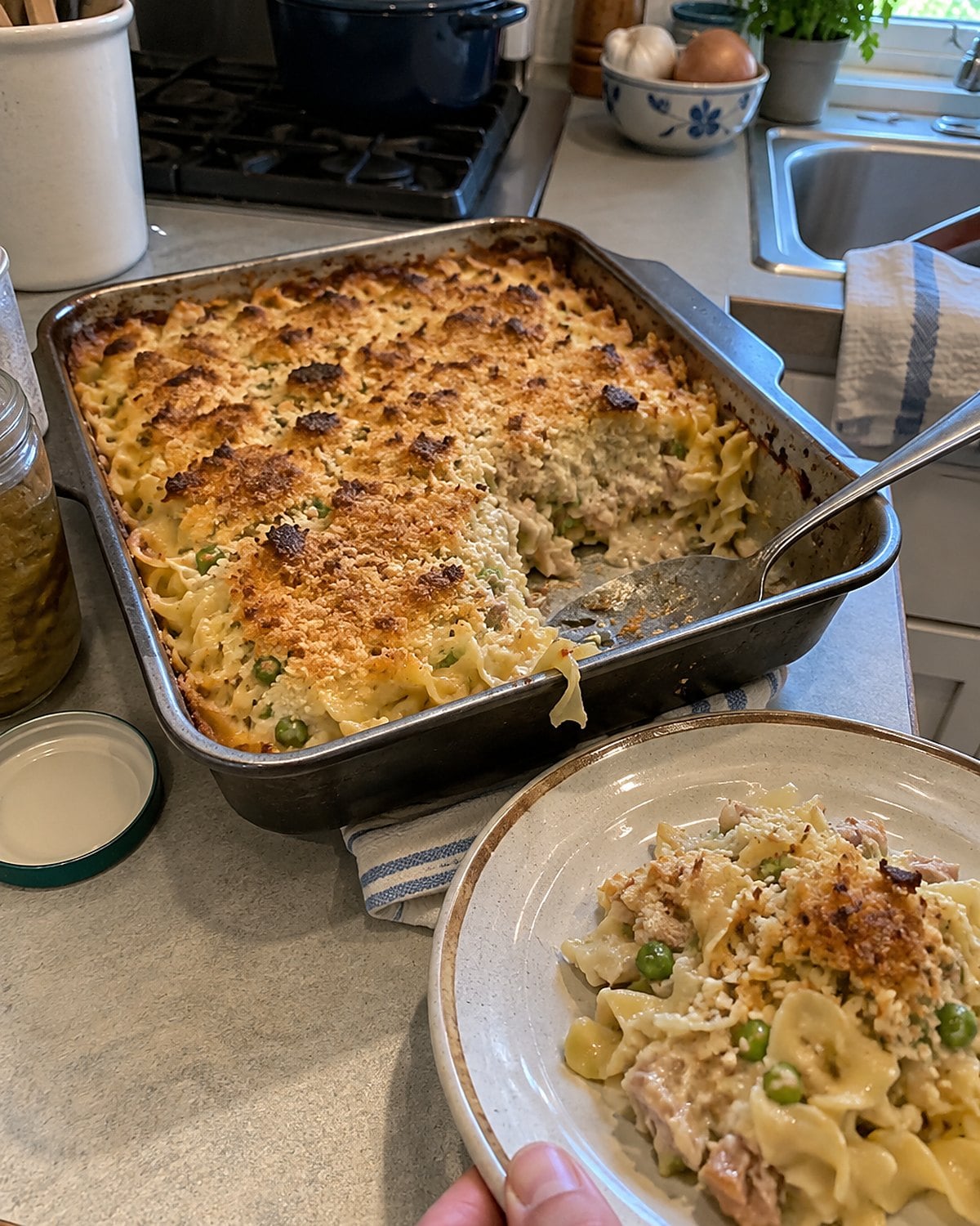 A small pan of tuna noodle casserole sits on a counter with a browned edge and a spoonful missing.