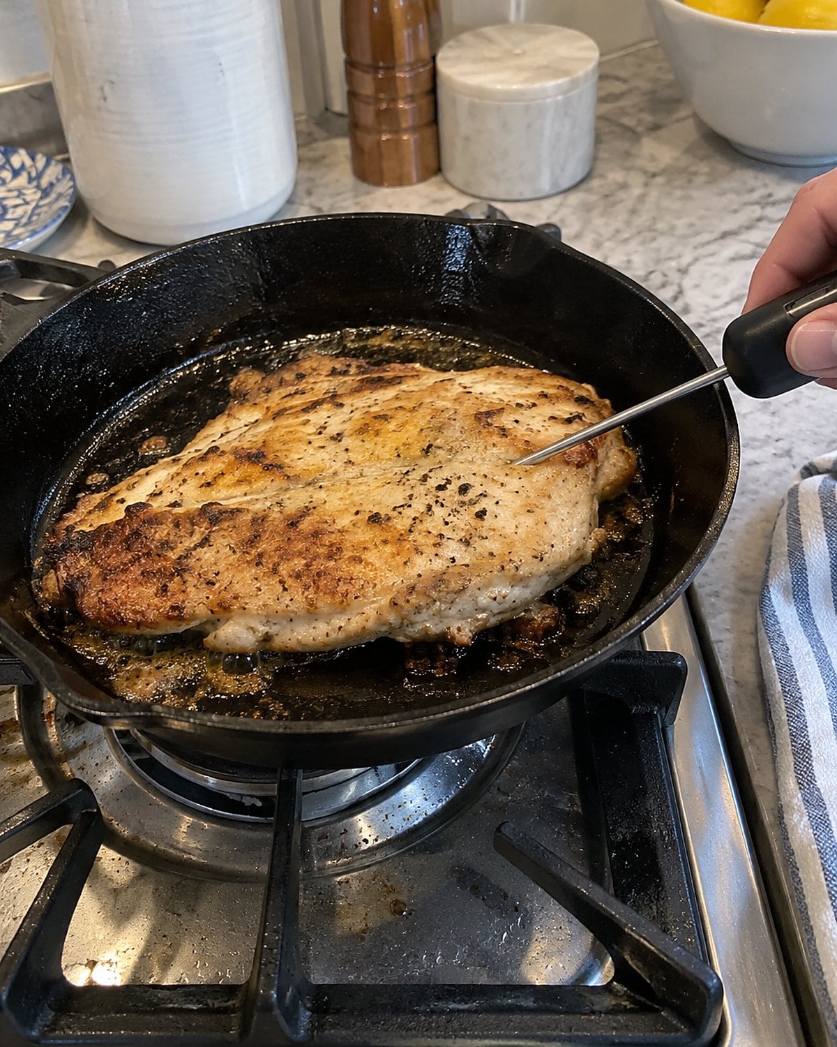 A thermometer enters the side of a chicken cutlet in a skillet on the stove.