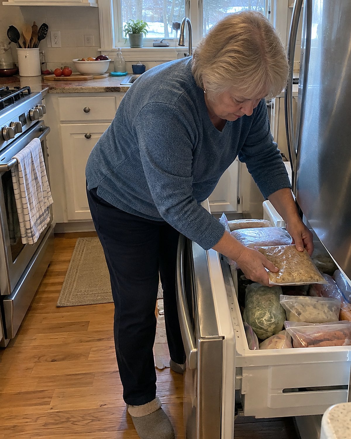 A hand slides a flat freezer bag of cooked food into a crowded freezer drawer.