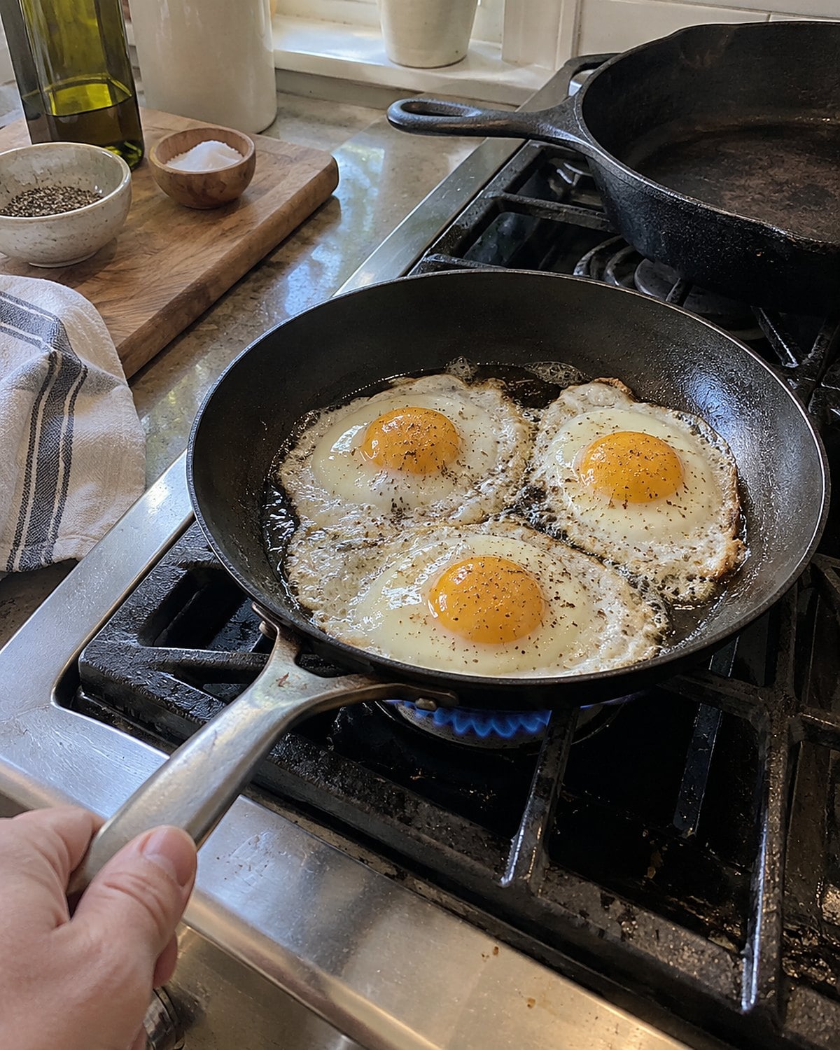 A small skillet sits on a lit burner beside a larger cast-iron pan on the stove.