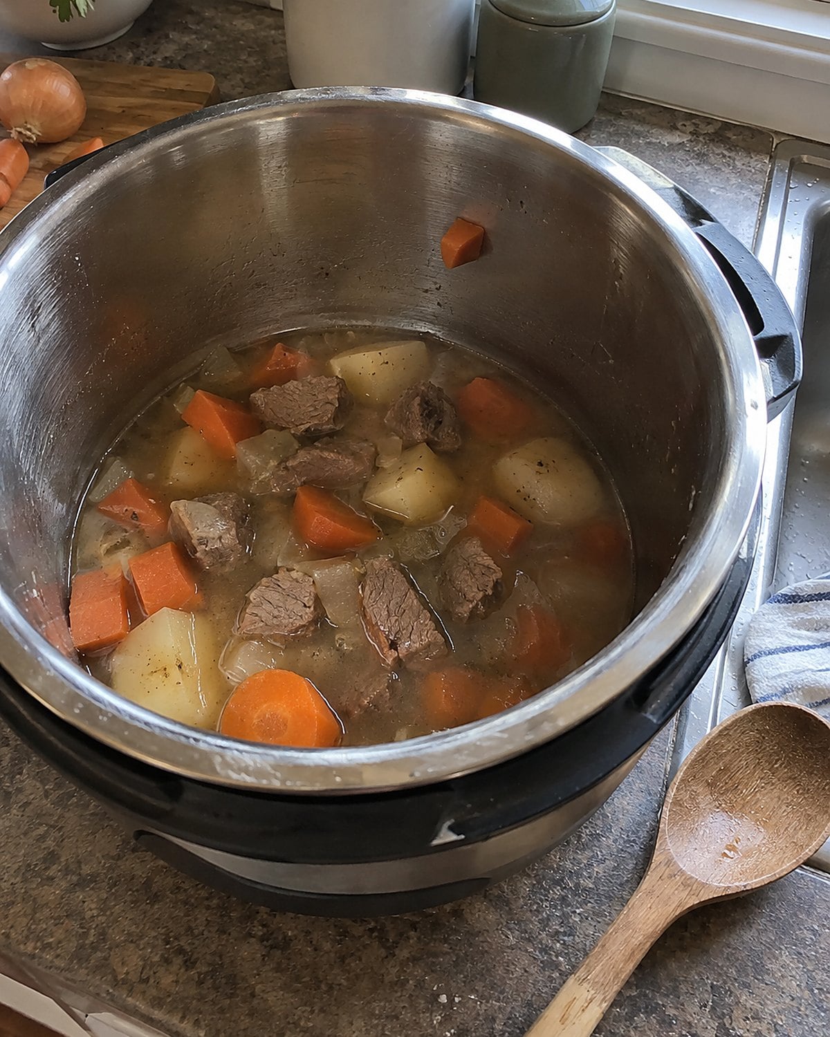An Instant Pot insert holds a small amount of stew ingredients and thin broth on the counter.