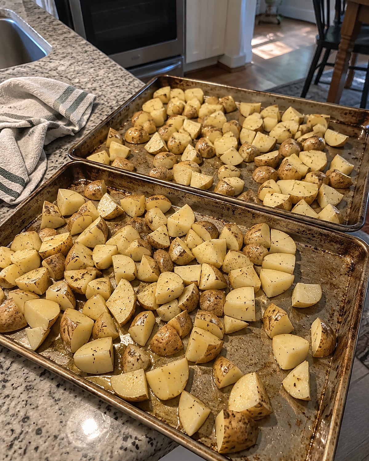 Cut potatoes spread across two worn sheet pans beside the oven.