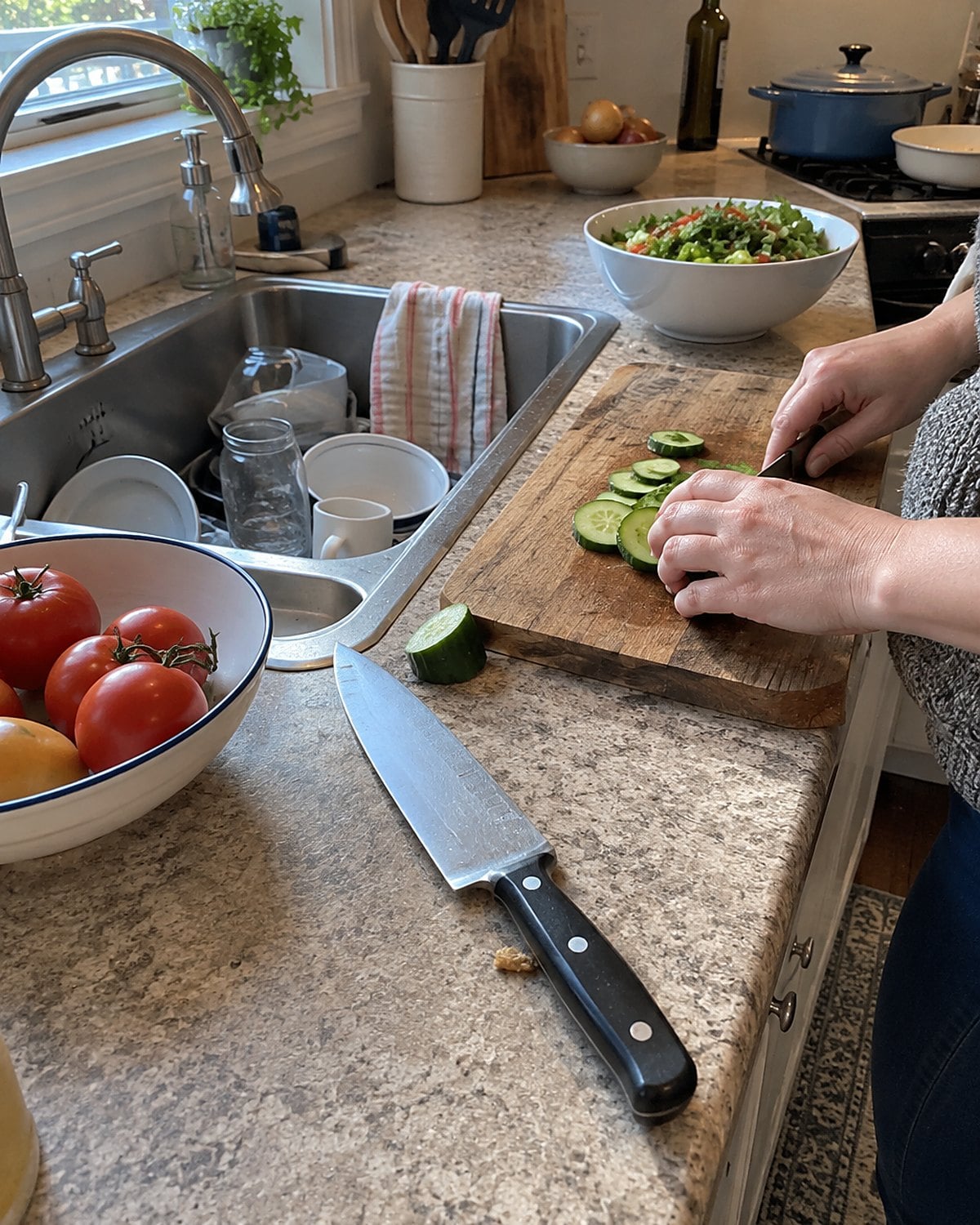 A chefโs knife lying flat on the counter beside a sink full of dishes.