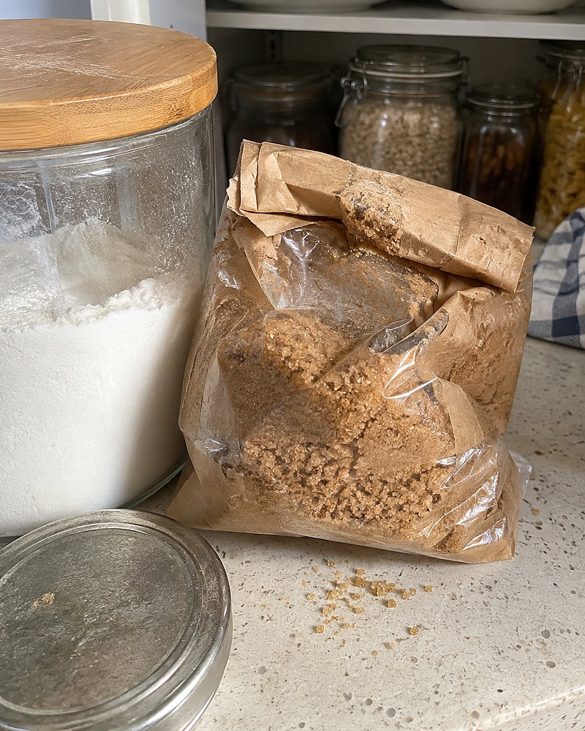 A crumpled bag of brown sugar beside a lidded container on the pantry counter.