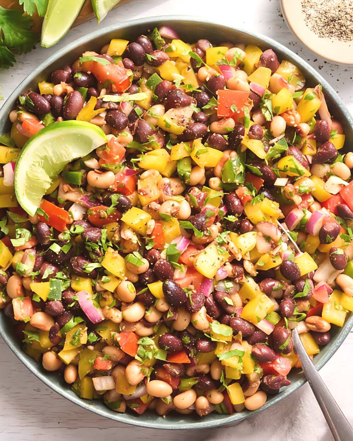 Colorful, fresh Cowboy Caviar packed with black beans, black-eyed peas, chopped bell peppers, tomatoes, onions, cilantro, and lime wedges, serving as vibrant last minute potluck ideas.
