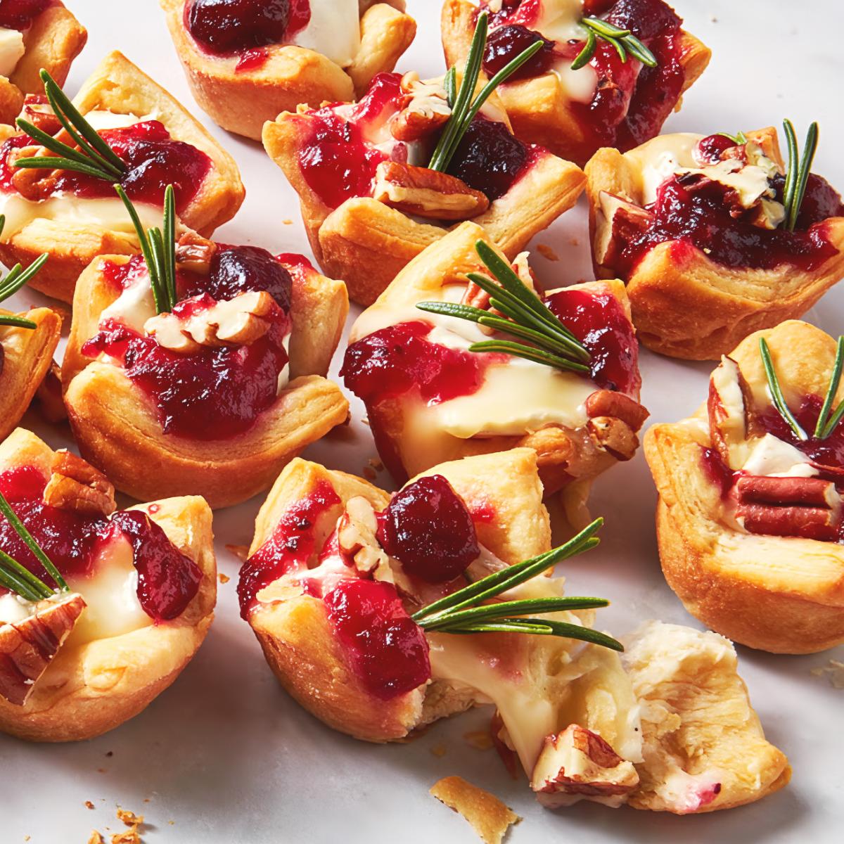 Warm cranberry brie bites garnished with fresh rosemary sprigs and pecans served as easy Thanksgiving finger food ideas.