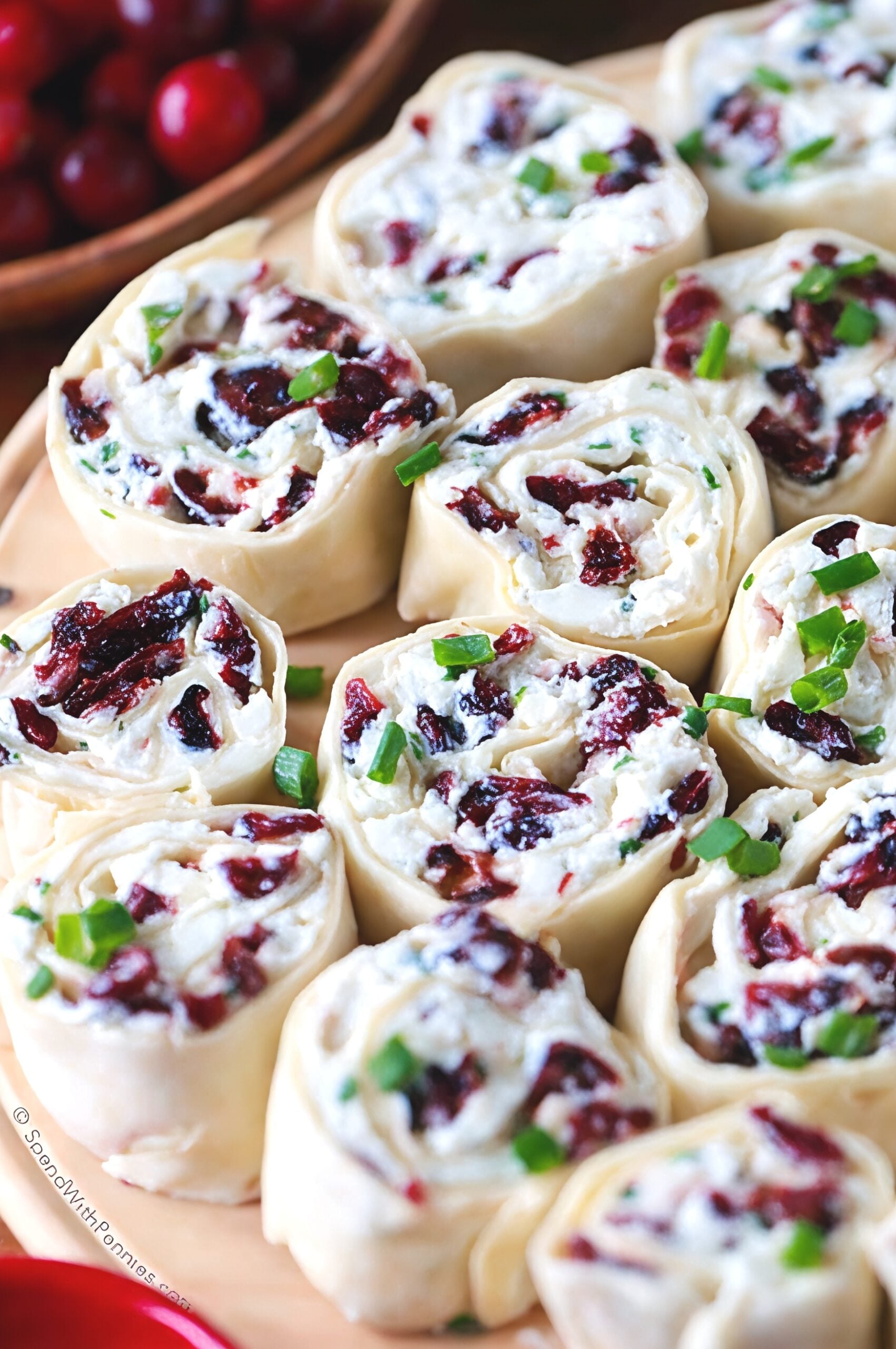 Tortilla roll-ups filled with cream cheese, feta, dried cranberries, and chopped green onions arranged on a cutting board as easy Thanksgiving finger food ideas.
