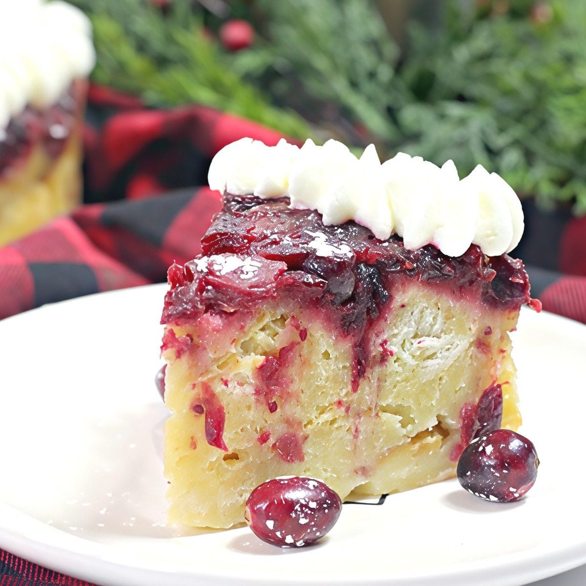 A slice of pressure cooker cranberry baked French toast topped with whipped cream and fresh cranberries on a white plate as Thanksgiving breakfast ideas