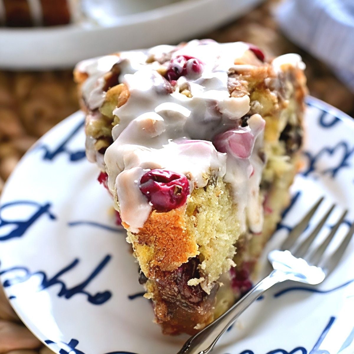 A slice of cranberry pecan coffee cake drizzled with white glaze and topped with fresh cranberries on a decorative white plate as Thanksgiving breakfast ideas.
