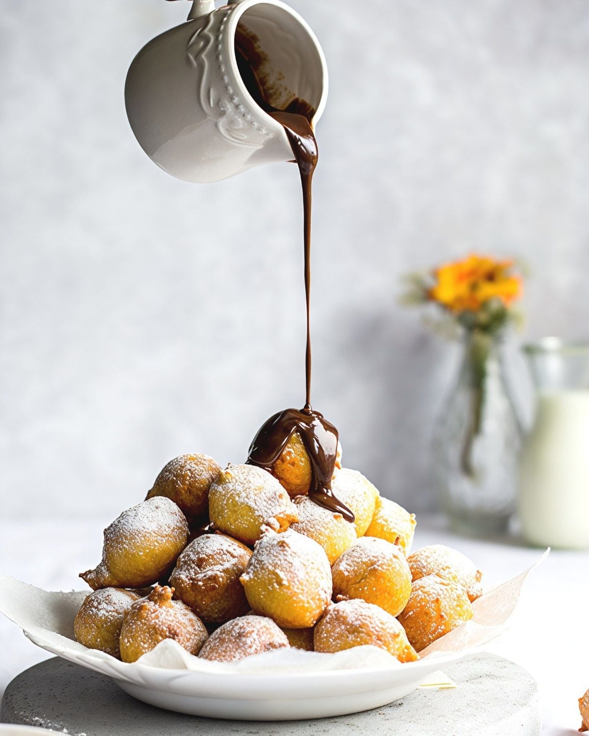 Golden-brown Croatian Fritule fritters dusted with powdered sugar and drizzled with warm chocolate sauce, served as a traditional European Christmas dessert.