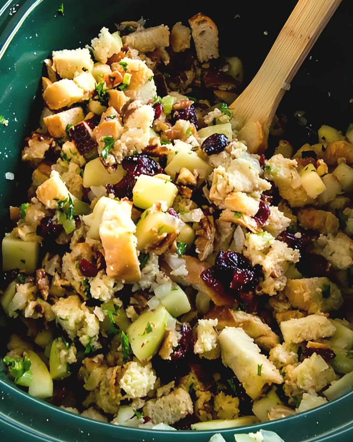 A green slow cooker filled with warm apple cranberry stuffing and a wooden spoon, making it one of the best crockpot thanksgiving sides.