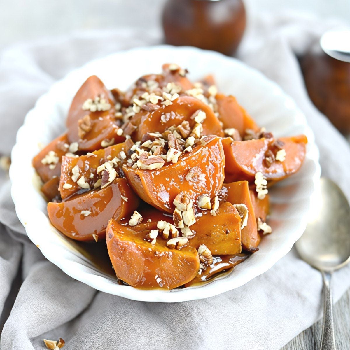 A white bowl filled with slow cooker candied sweet potatoes topped with chopped pecans, served as one of the best crockpot thanksgiving sides.