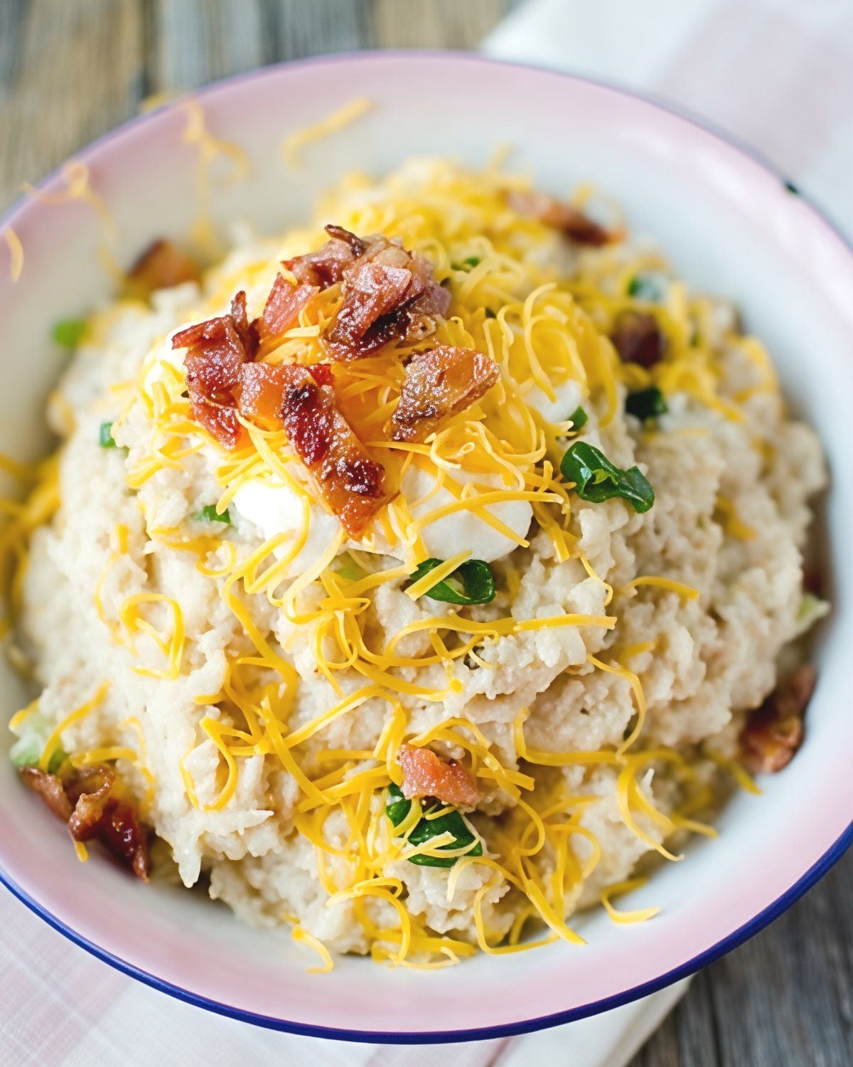 A bowl of creamy slow cooker cauliflower topped with shredded cheddar cheese, crispy bacon bits, and chopped green onions, featured as one of the best crockpot thanksgiving sides.