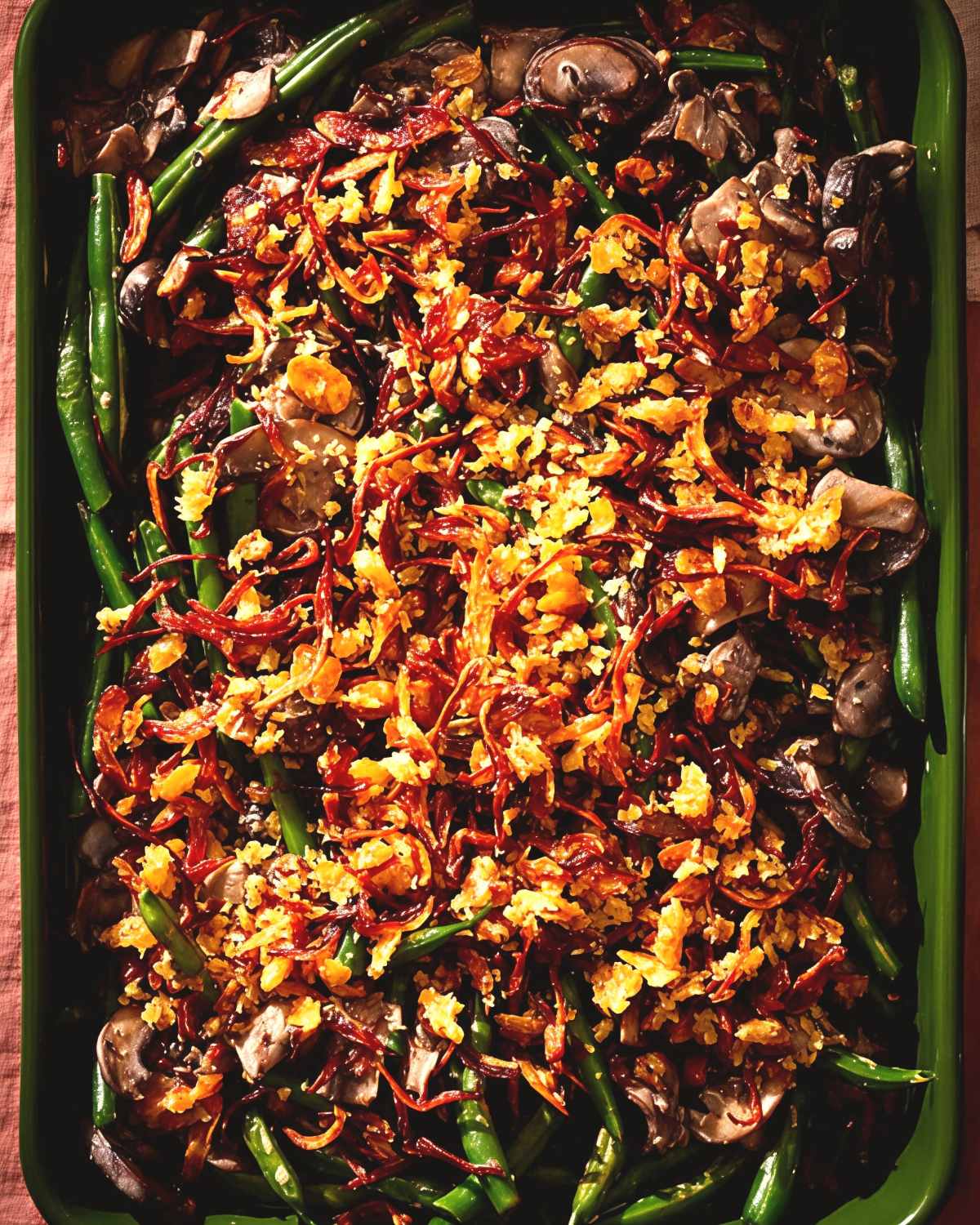 A green baking dish filled with fresh green beans, sliced mushrooms, and crispy fried onions, perfect for crockpot thanksgiving sides.