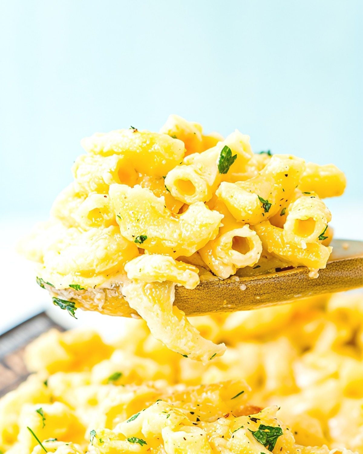 A wooden spoon lifting a scoop of rich and creamy mac and cheese garnished with chopped parsley, perfect for crockpot thanksgiving sides.